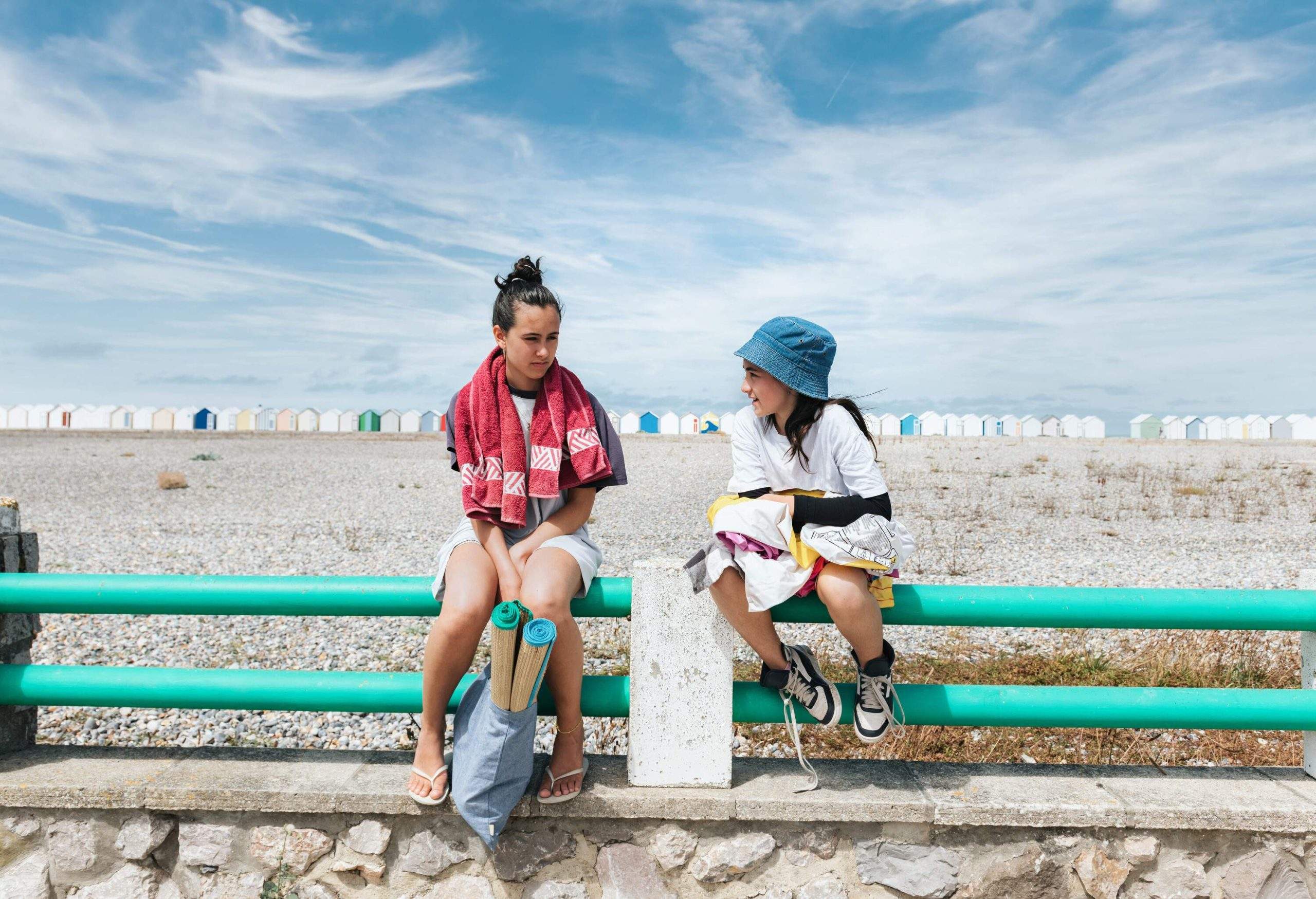 teenage girl and little sister with bathing equipment sitting together on balustrade at pebble beach in France in Cayeux-sur-Mer, France