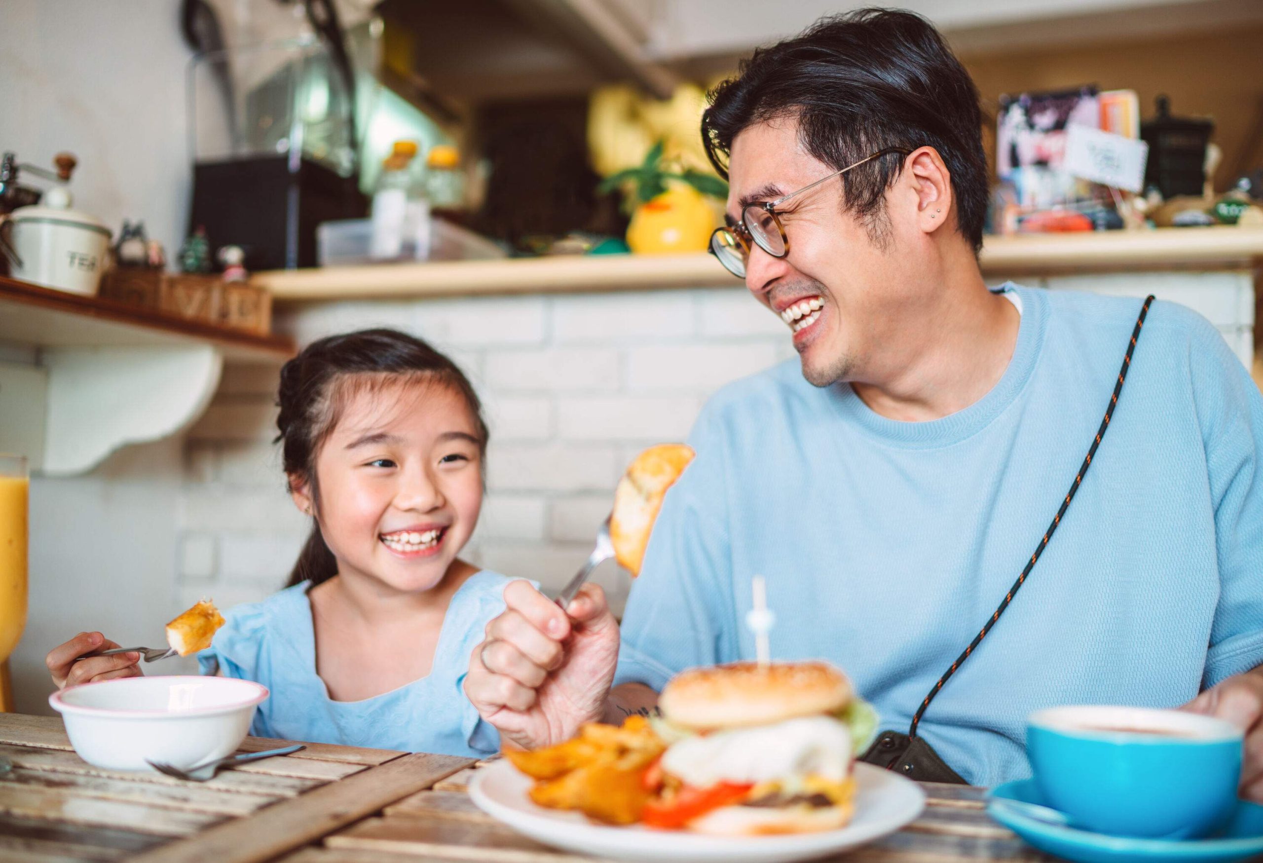 A father and daughter smile at each other while having burger in a restaurant.