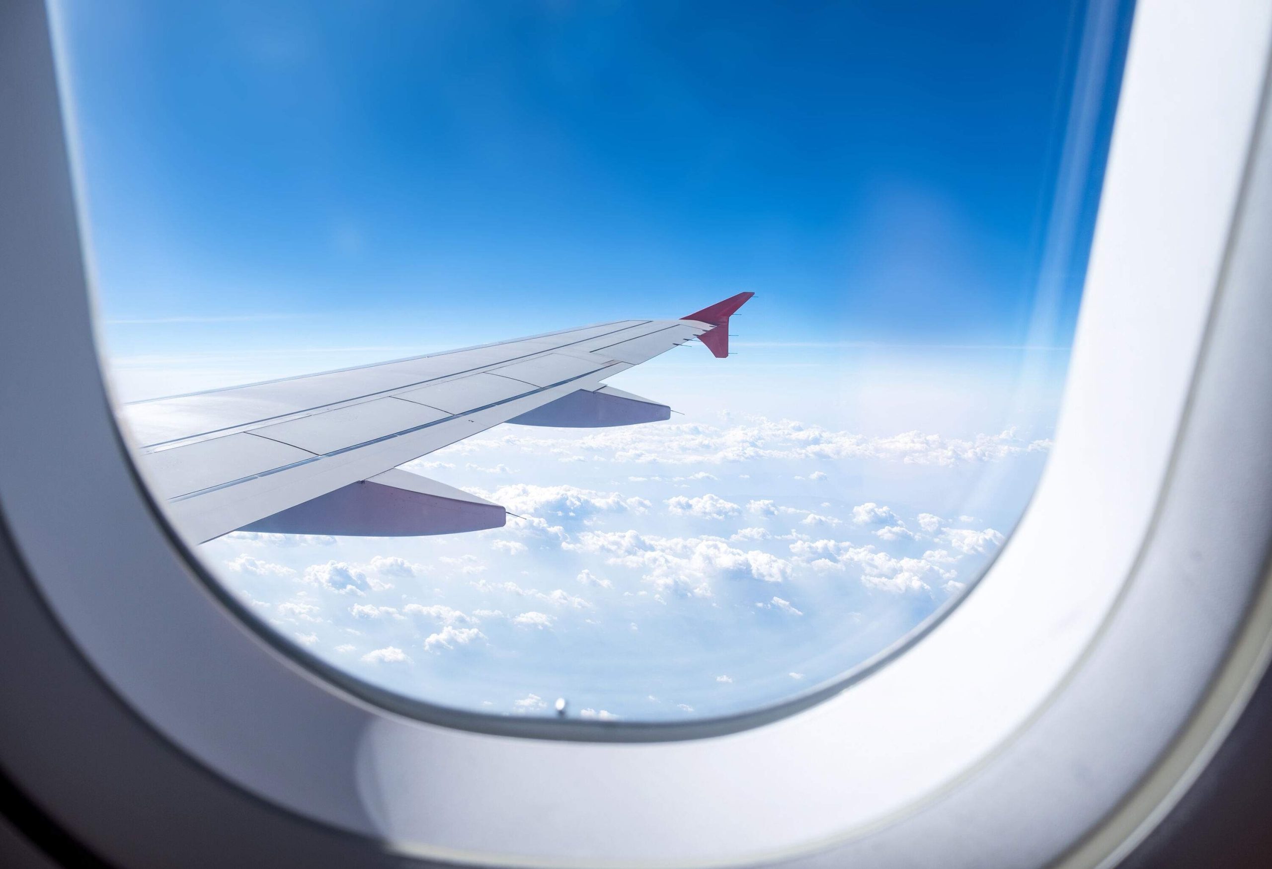 A plane in flight, with one of its wings visible through the window and a deep blue sky in the background.