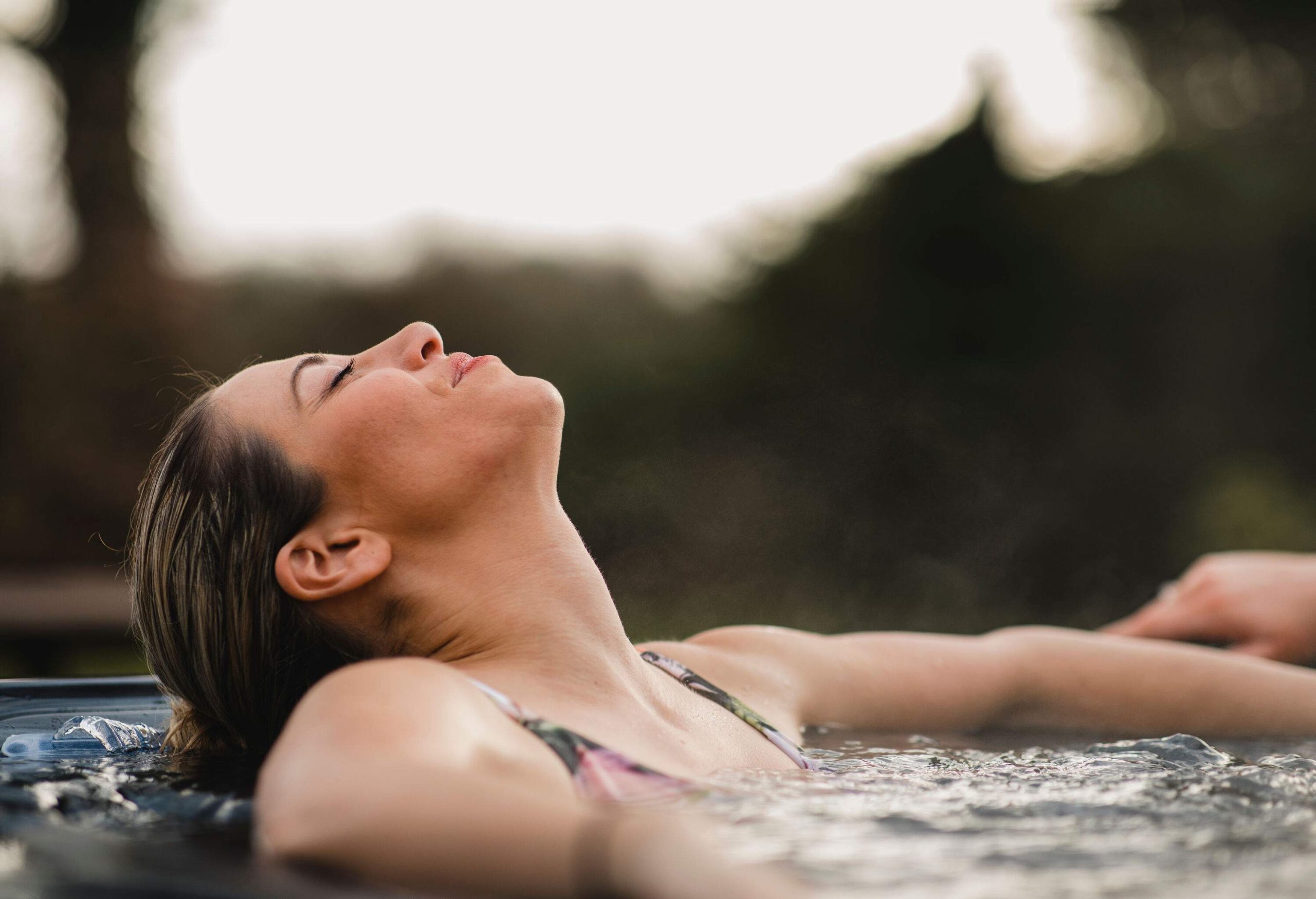 a woman leaning her head back while sitting in a hot tub outside