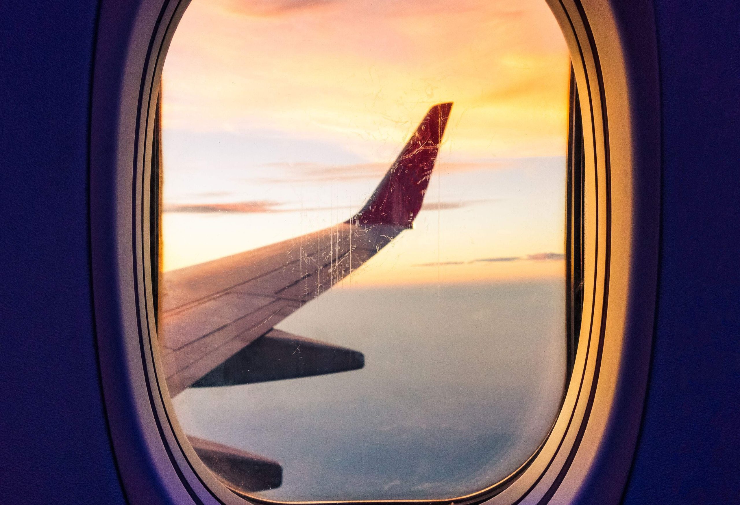 The aircraft wing against a scenic sunset sky viewed from the plane's window.