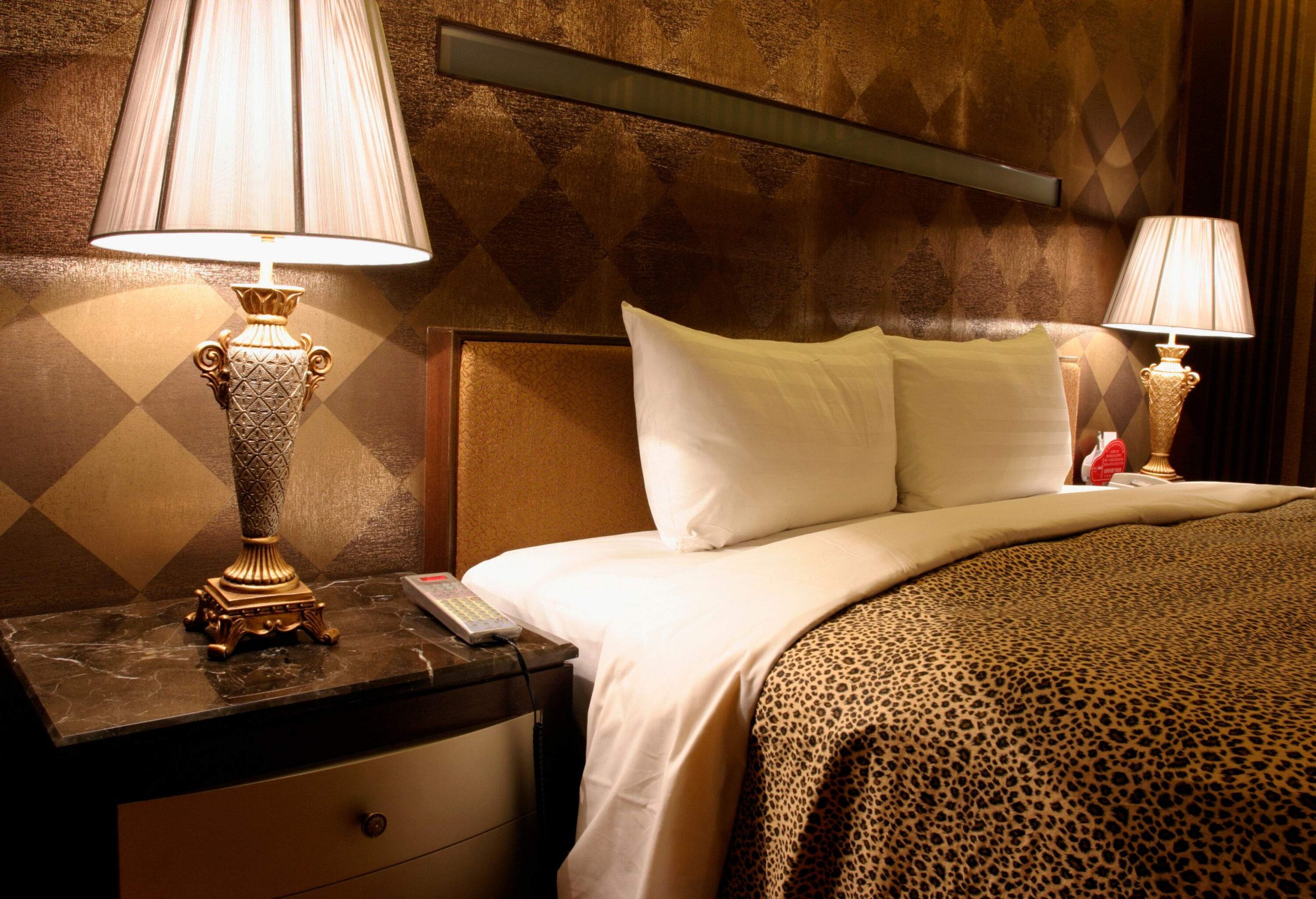 A cosy hotel bedroom adorned with a leopard print bedsheet, accentuated by warmly illuminated bedside lamps.