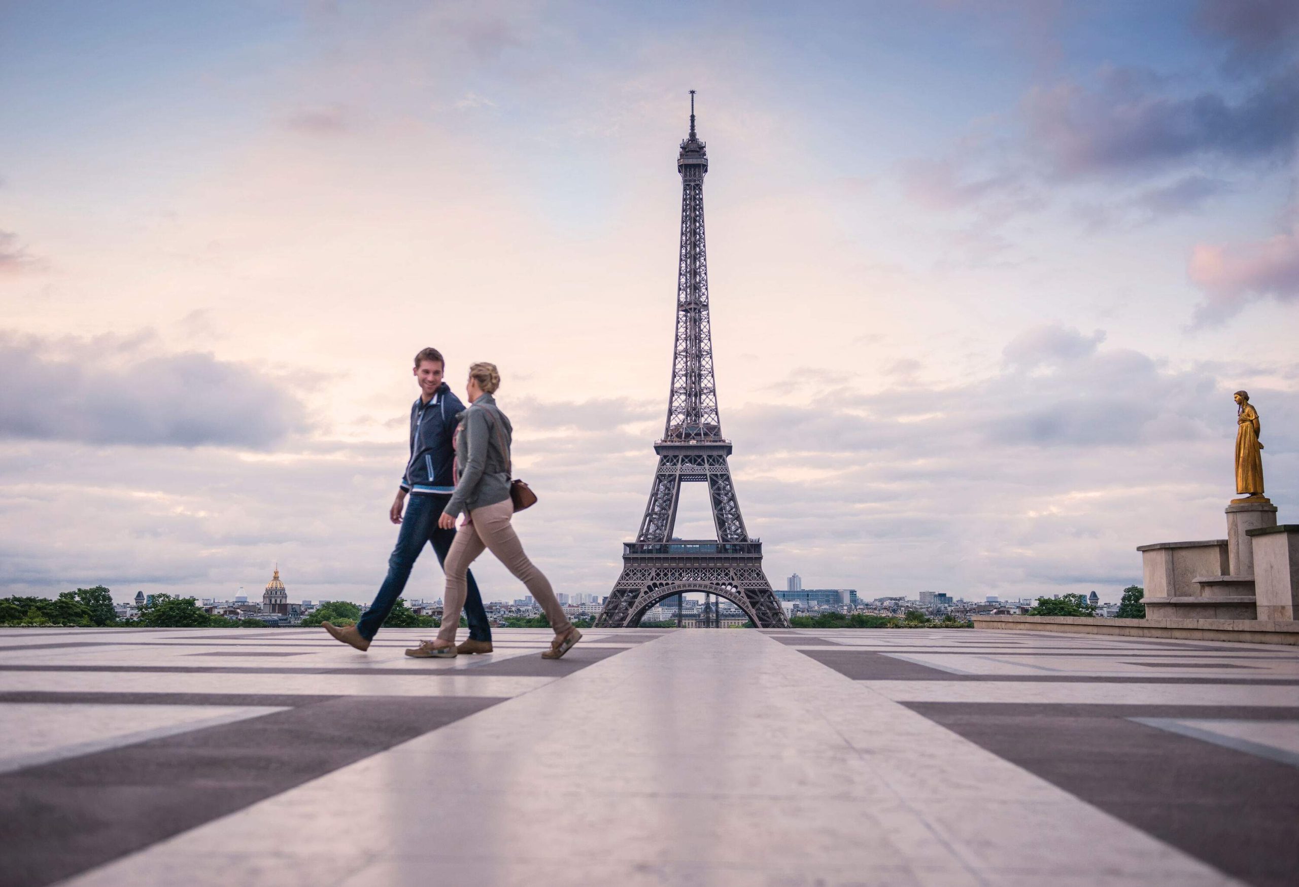 A happy couple walks on a platform with a view of the majestic Eifel Tower, captured against the scenic twilight.