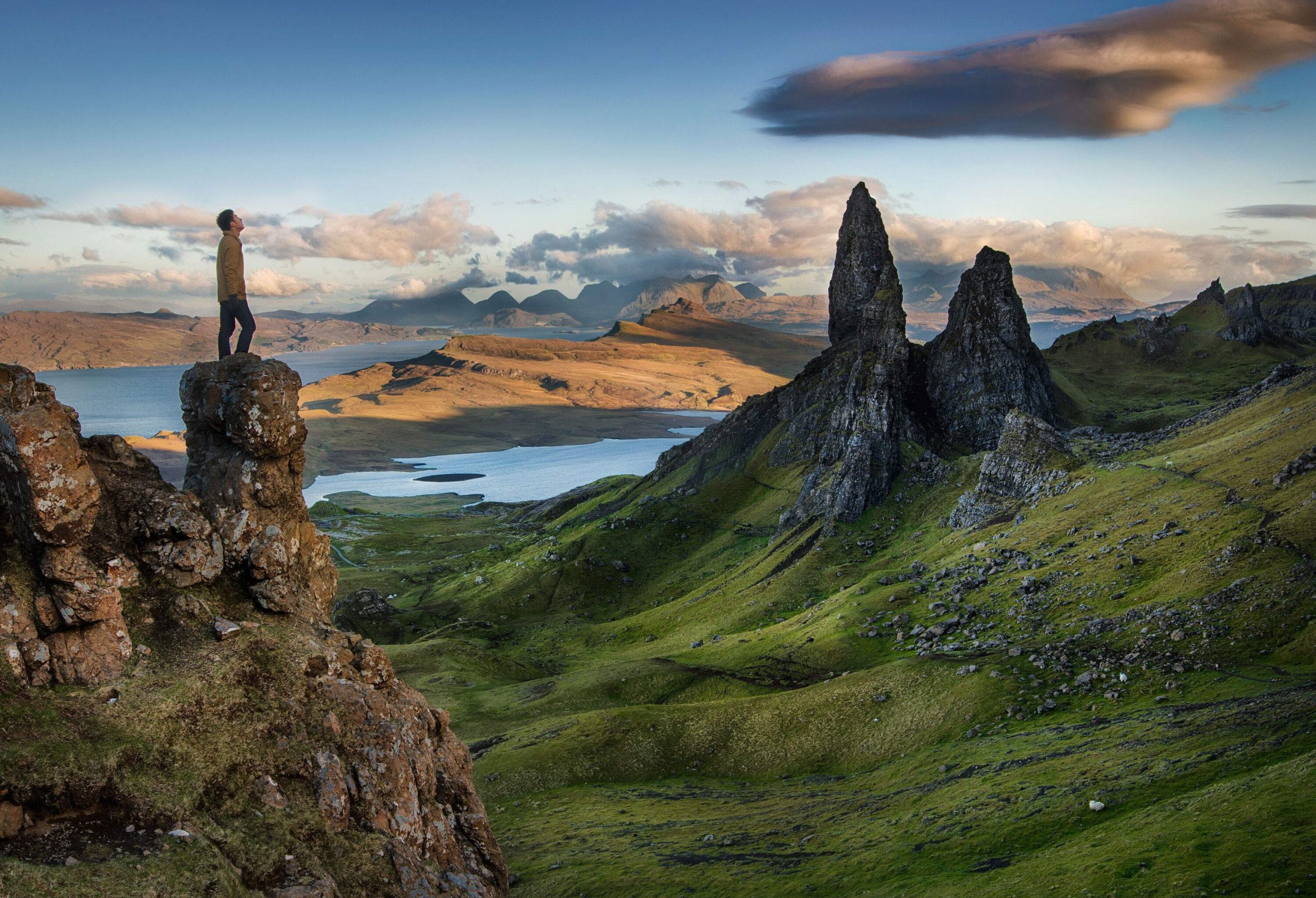 A man looking up to the sky as he stands on a rock pillar over plateaus and pinnacles of rock.