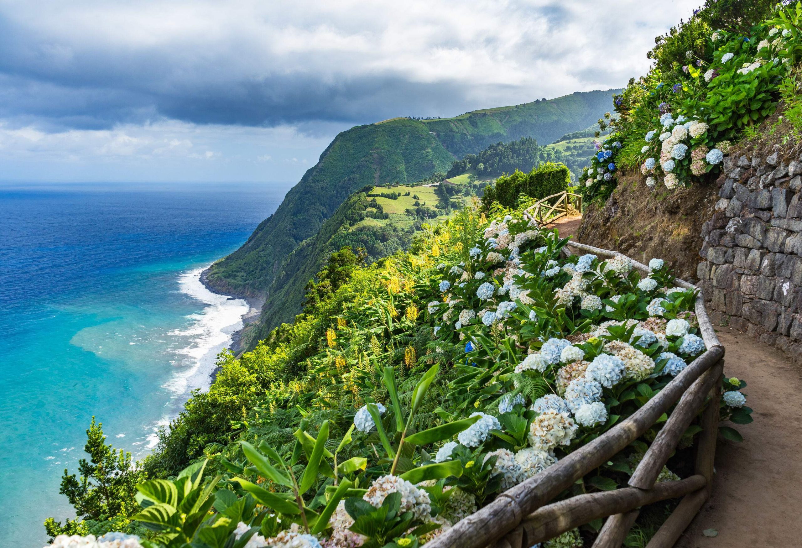 A walkway meandering alongside a steep slope, surrounded by lush greenery and offering breathtaking views of the expansive sea below.