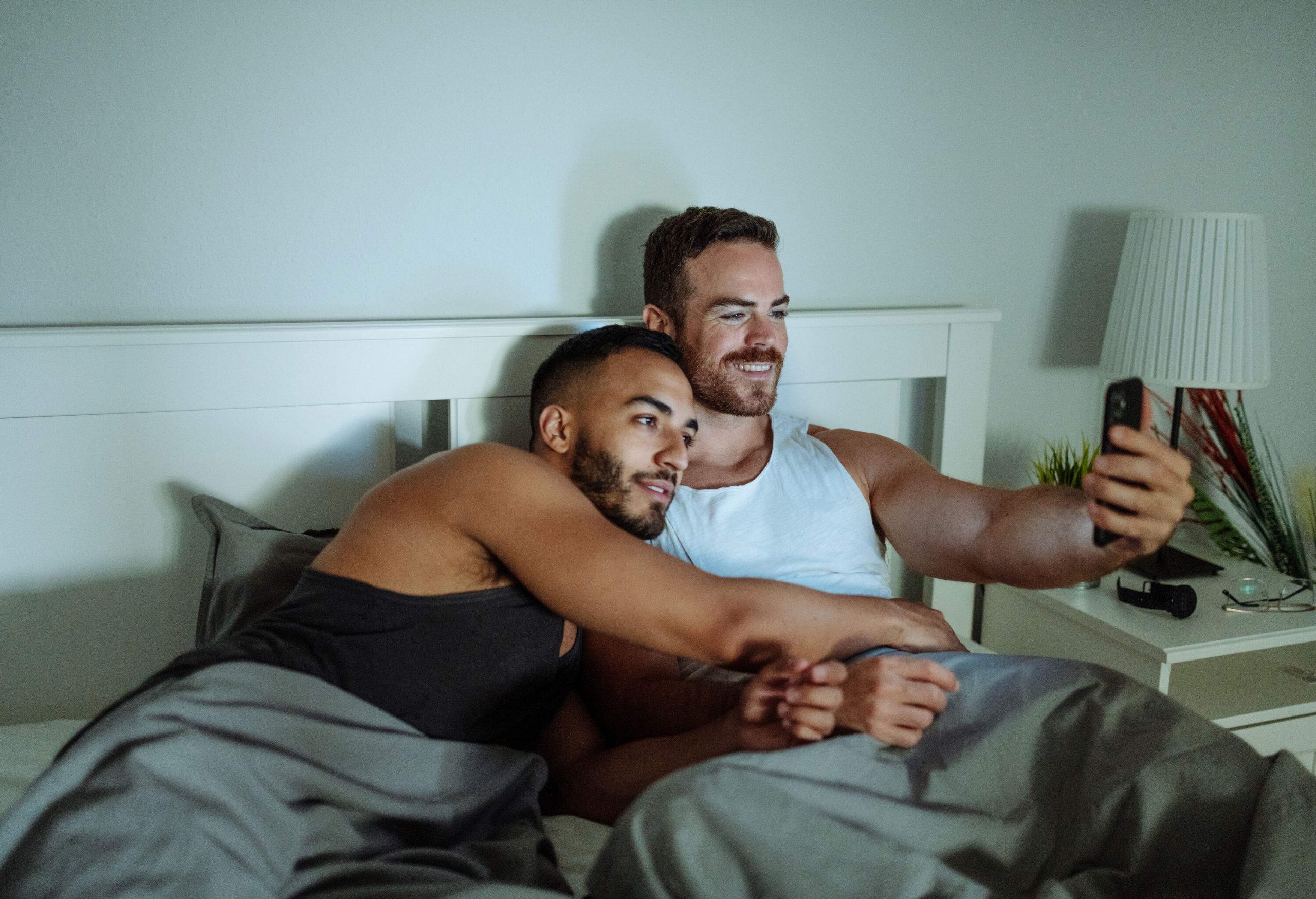 A sweet gay couple lying in bed and looking at a smart device.