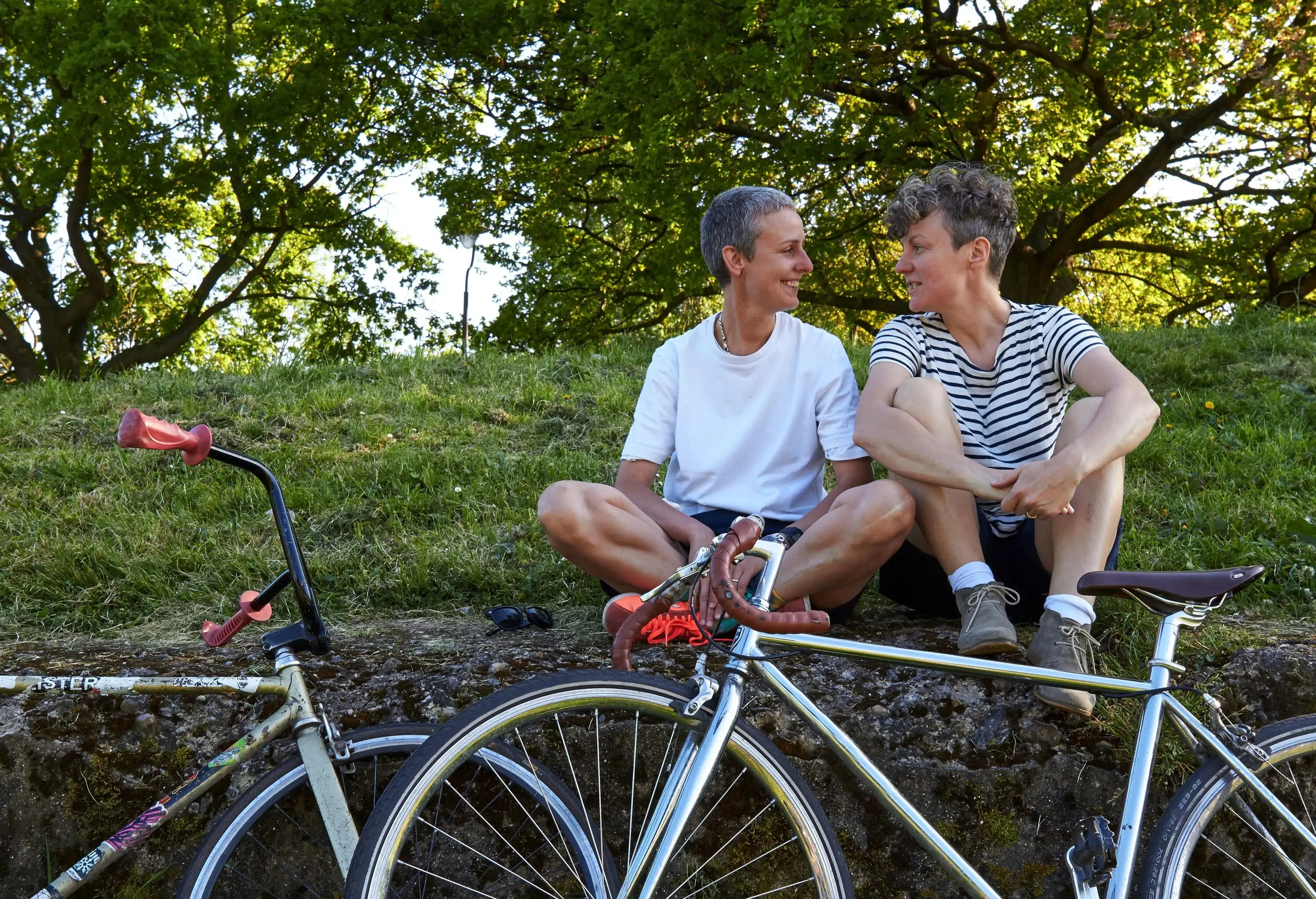 A female couple looking at each other sits behind their parked bicycles.