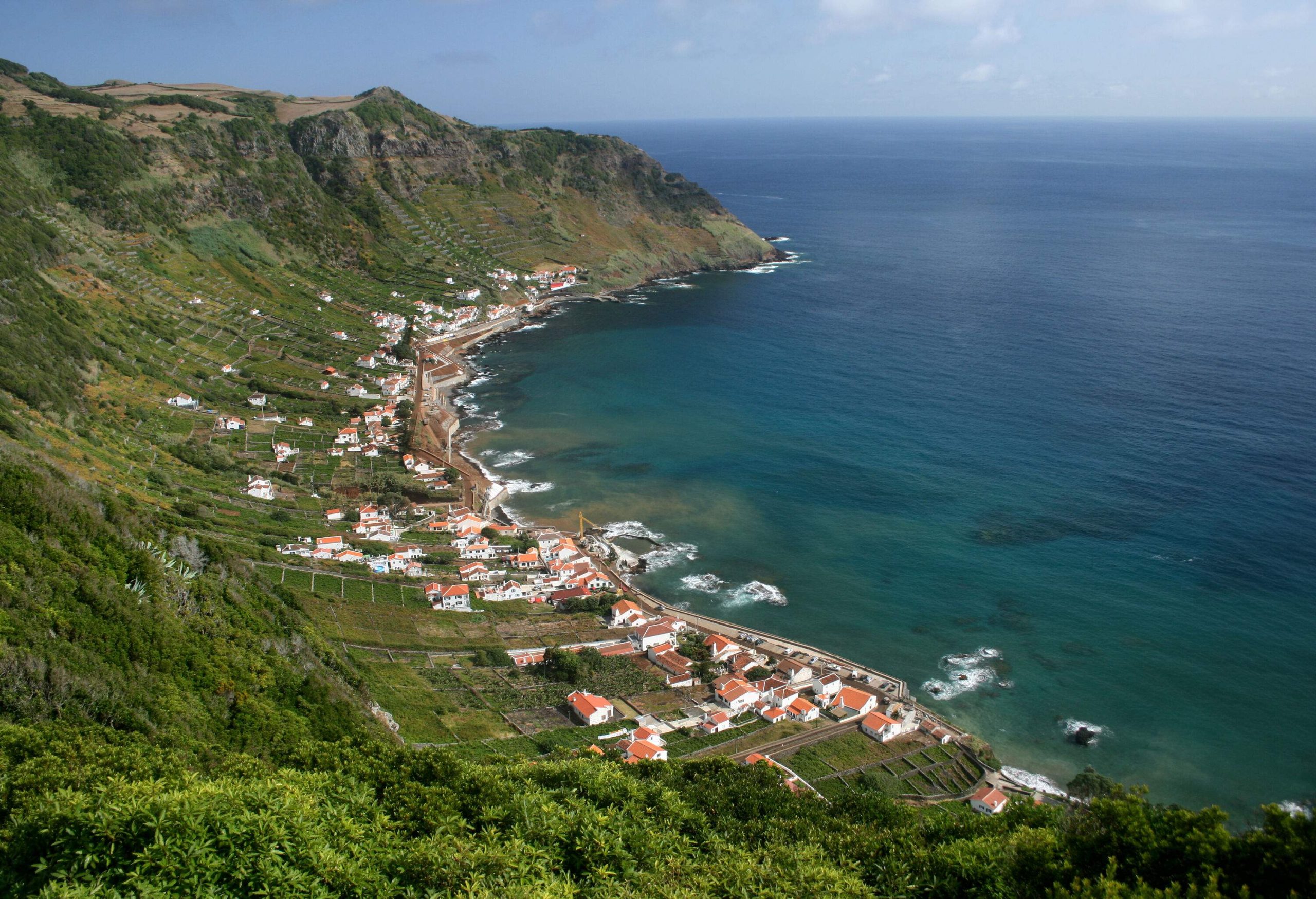 A coastal village at the base of forested slopes with sweeping views of a vast ocean.