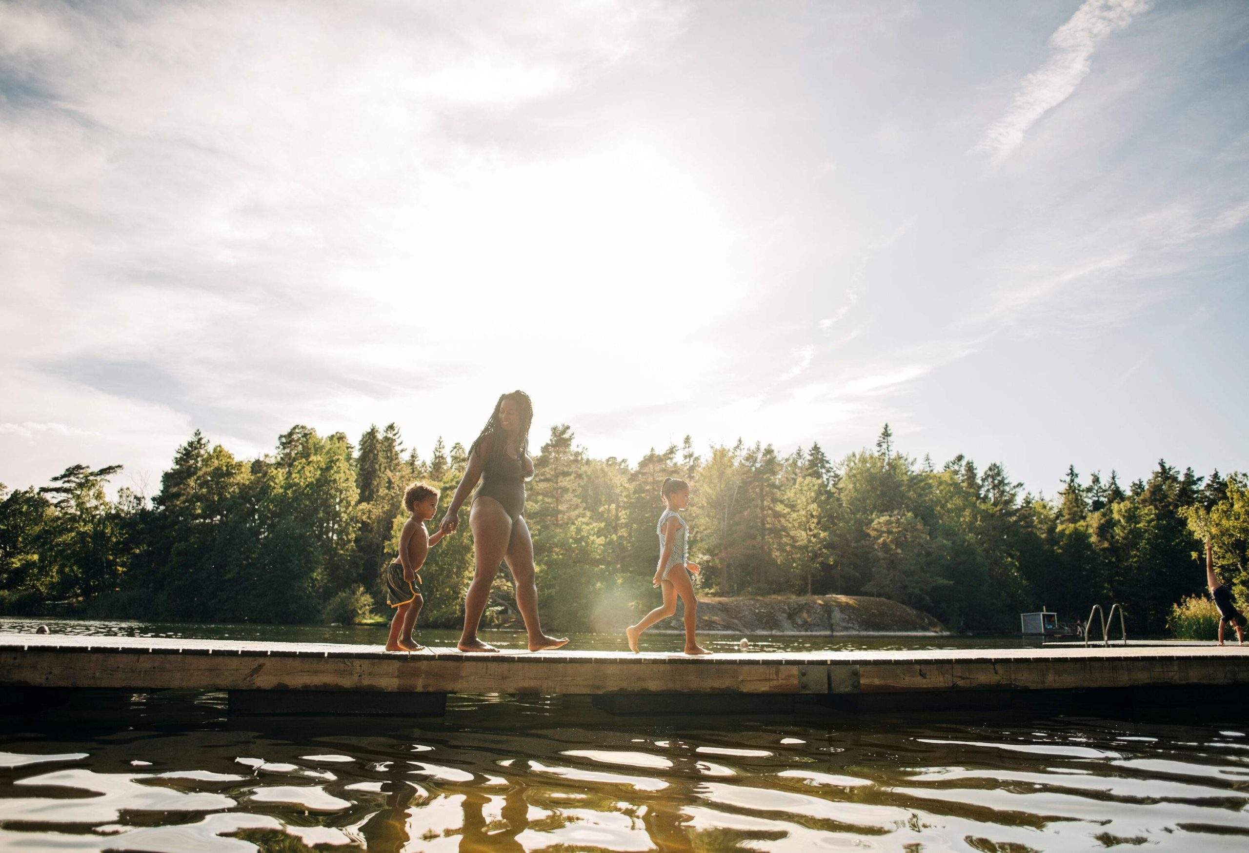 A woman and two children strolling on a boardwalk over a lake.