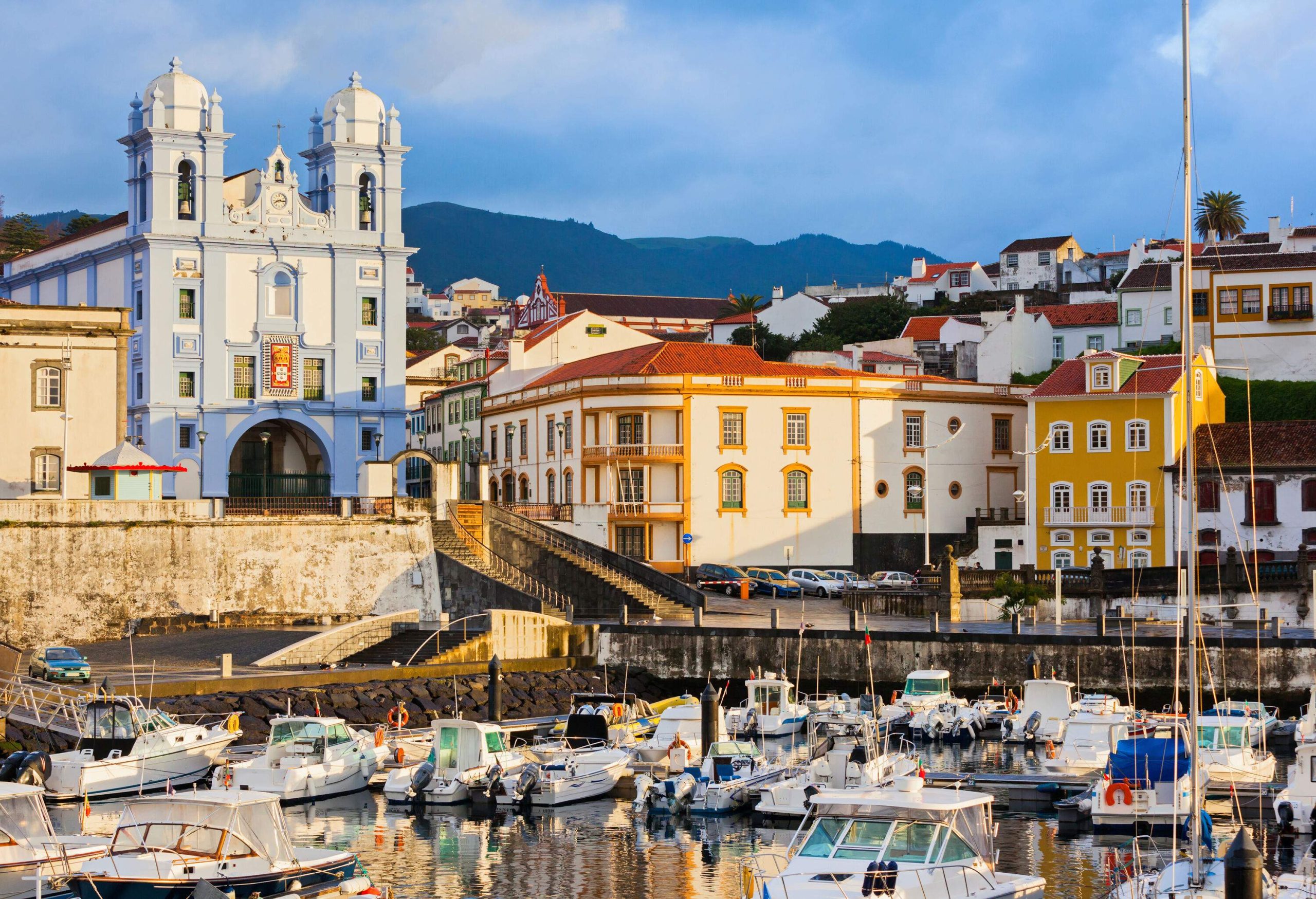 A port with boats docked alongside is complemented by vibrant waterfront buildings and a prominent church in the background.