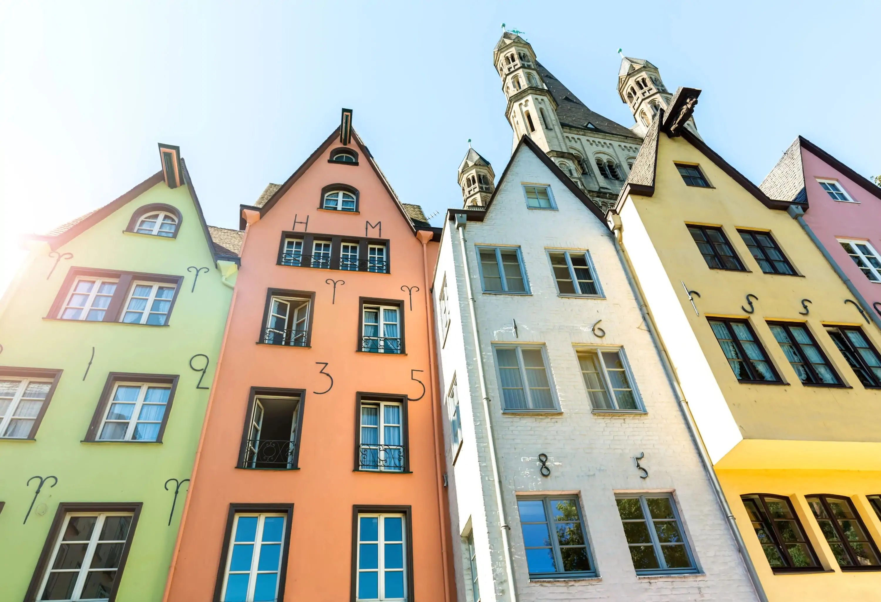 A row of colourful, narrow houses with church towers rising over them in the background.