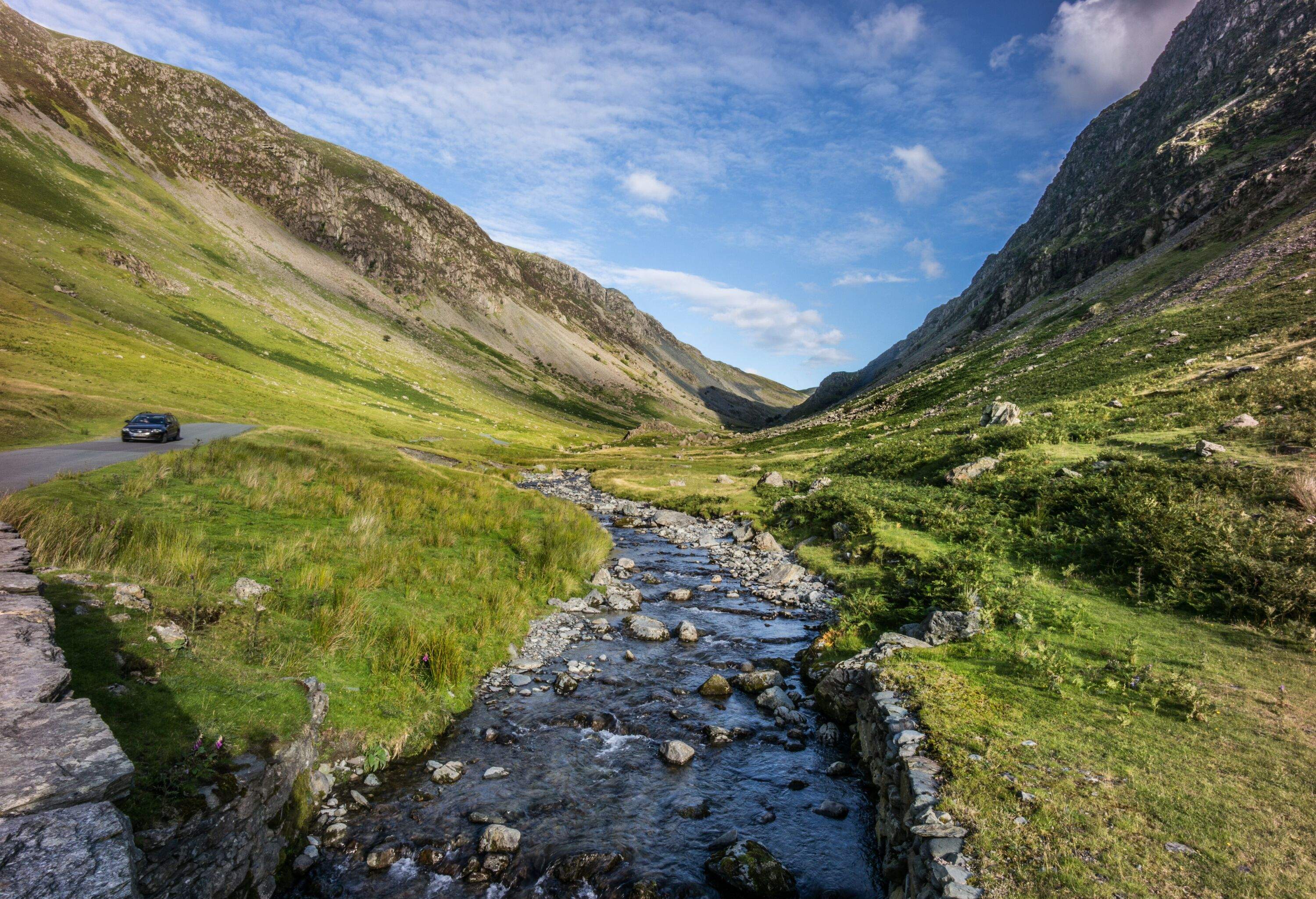 Small river bed in valley between two green mountains, and car passing by roadside