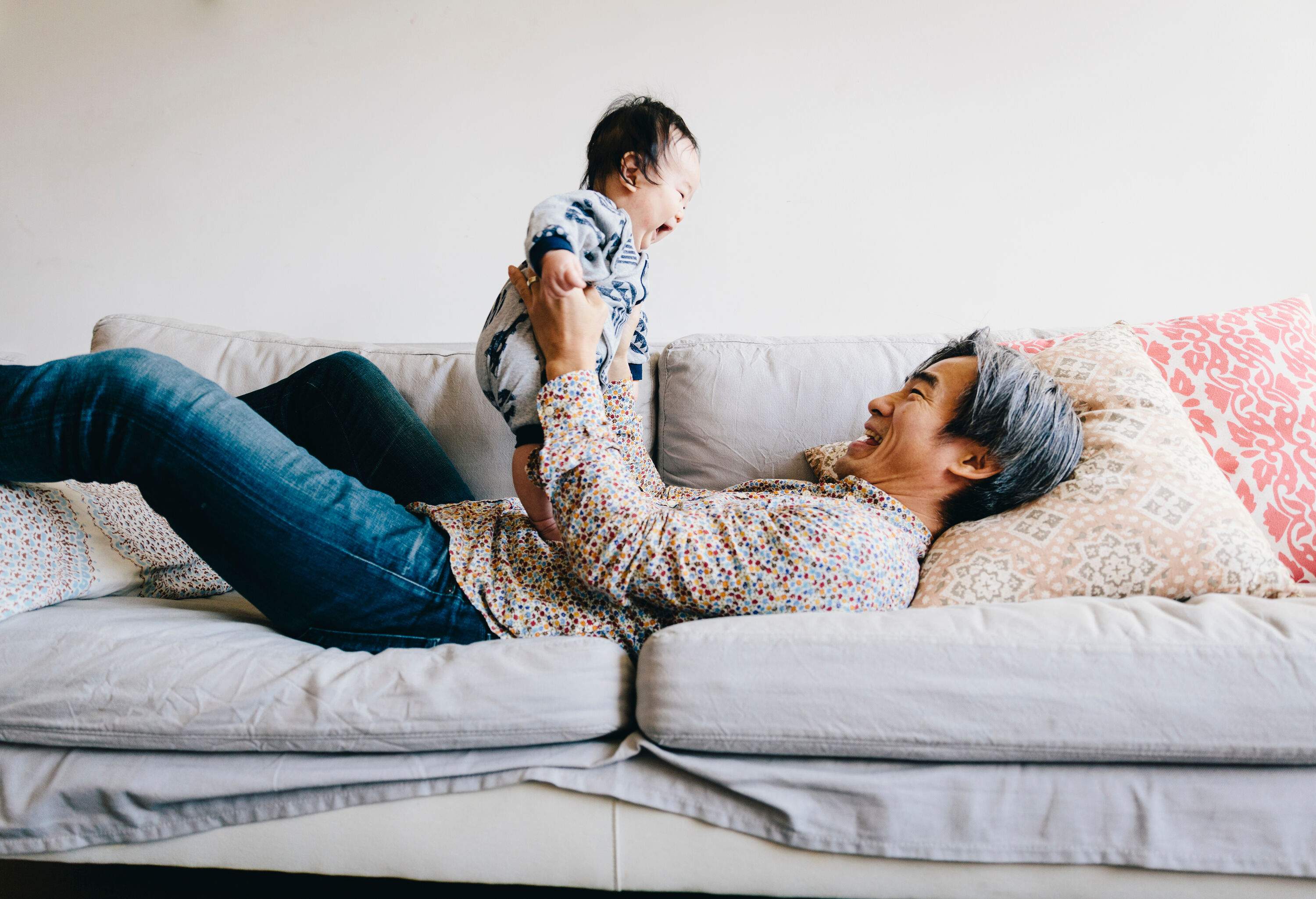 A grandfather lying on his back on a couch and playing with a baby.