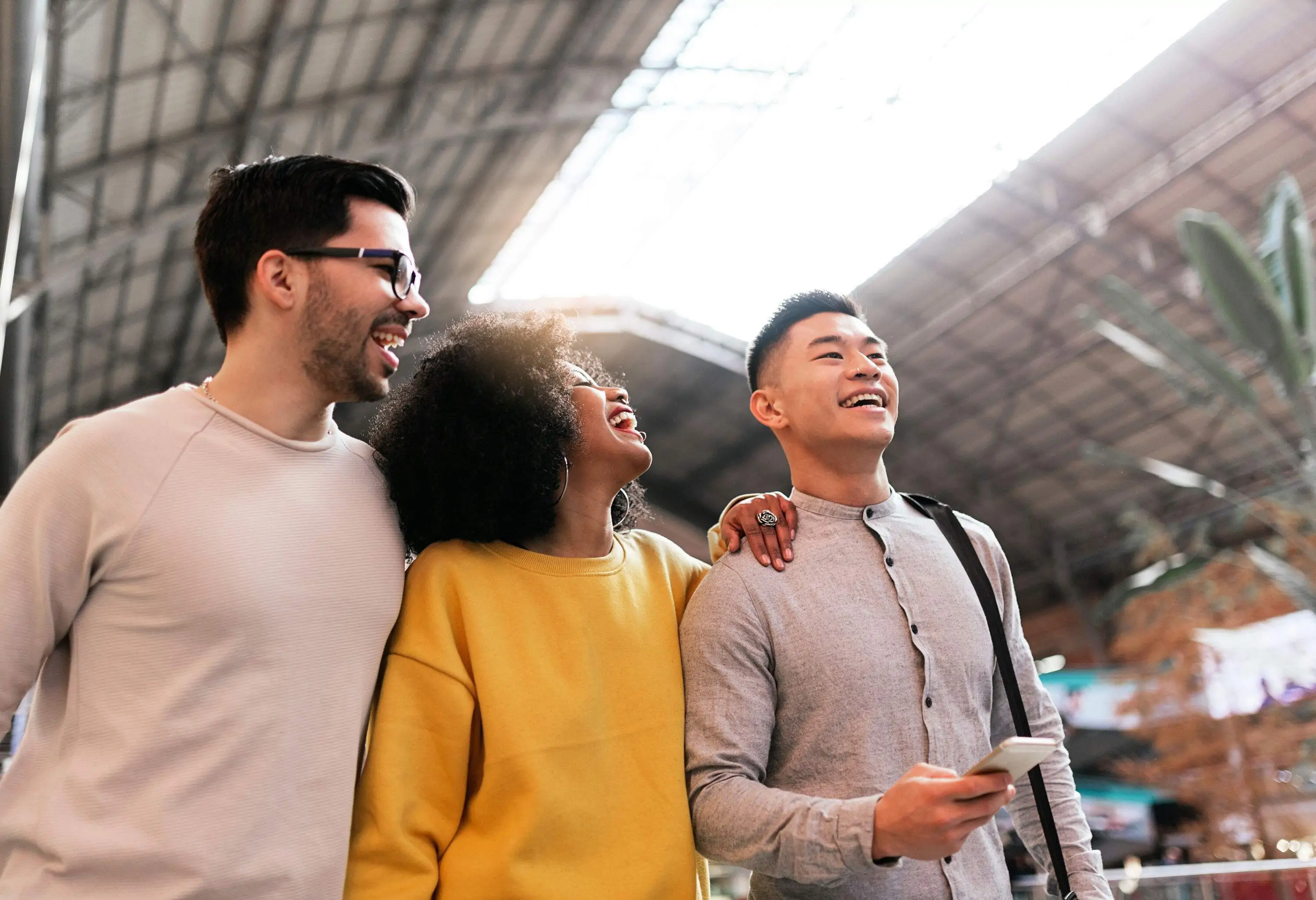 Three friends in comfortable clothes smile as they walk across a train station.