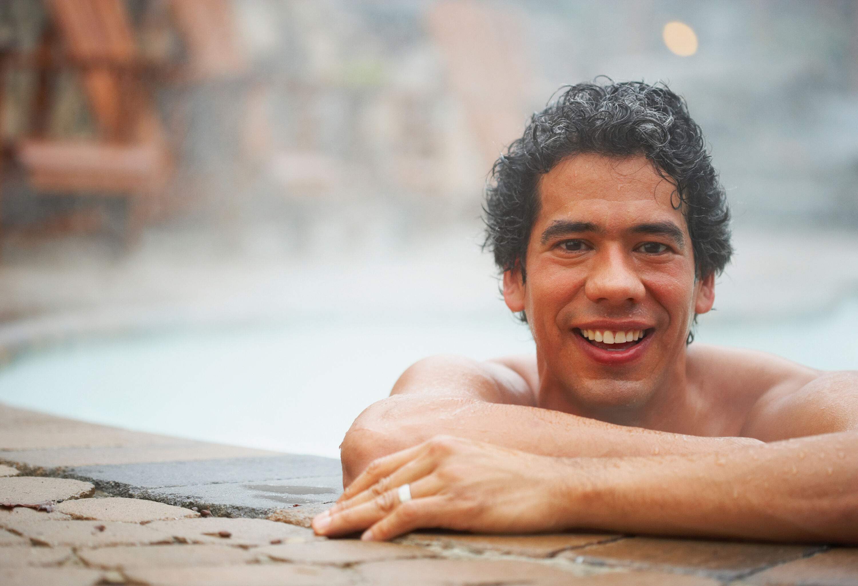 A smiling man leans his hands on the edge of the swimming pool.