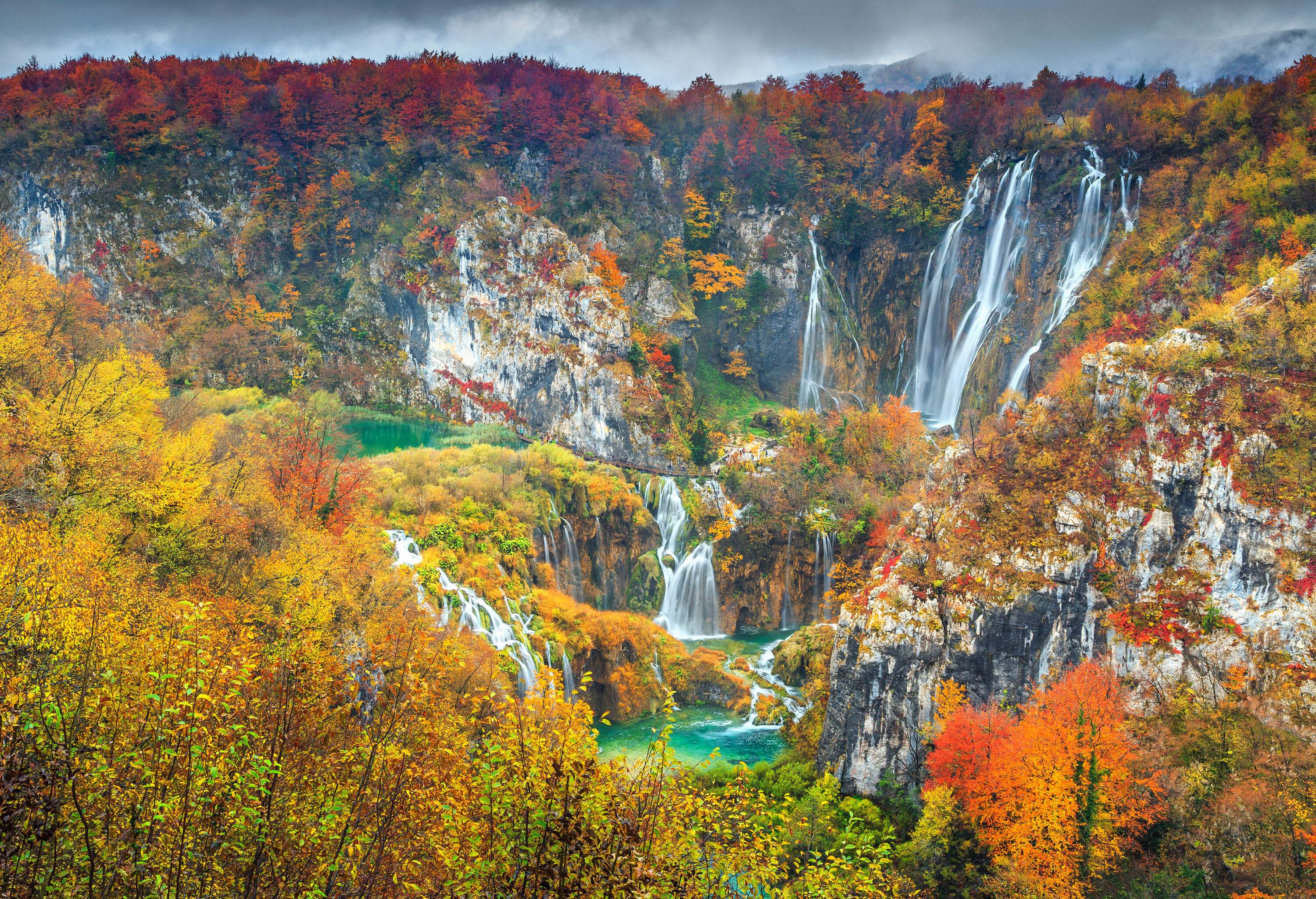 Picturesque waterfalls with water gushing over the rocks into a river surrounded by rocky mountains covered with autumn trees.