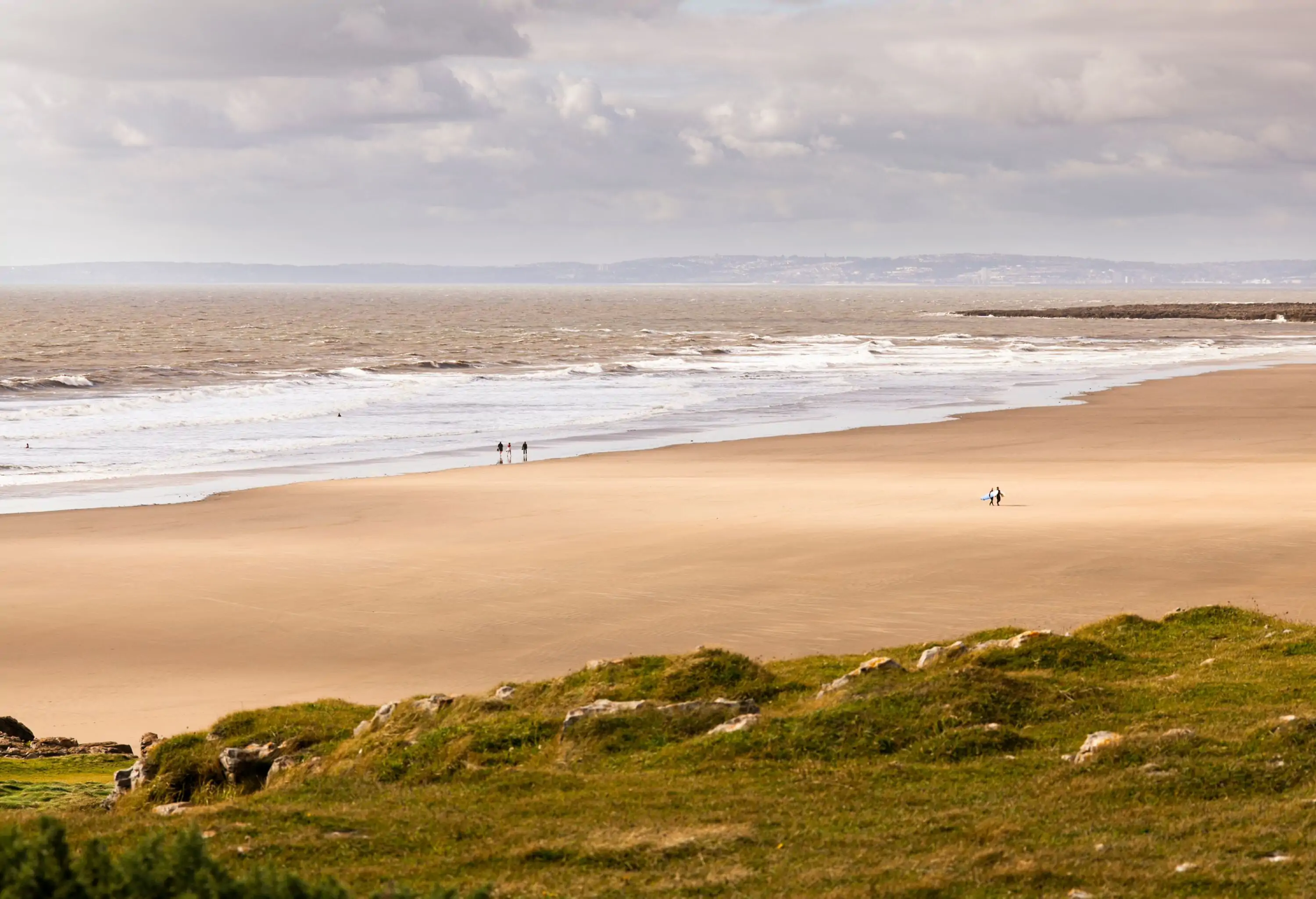 Wide sandy beach with people seen from afar from the top of a grassy mountain on an overcast windy day