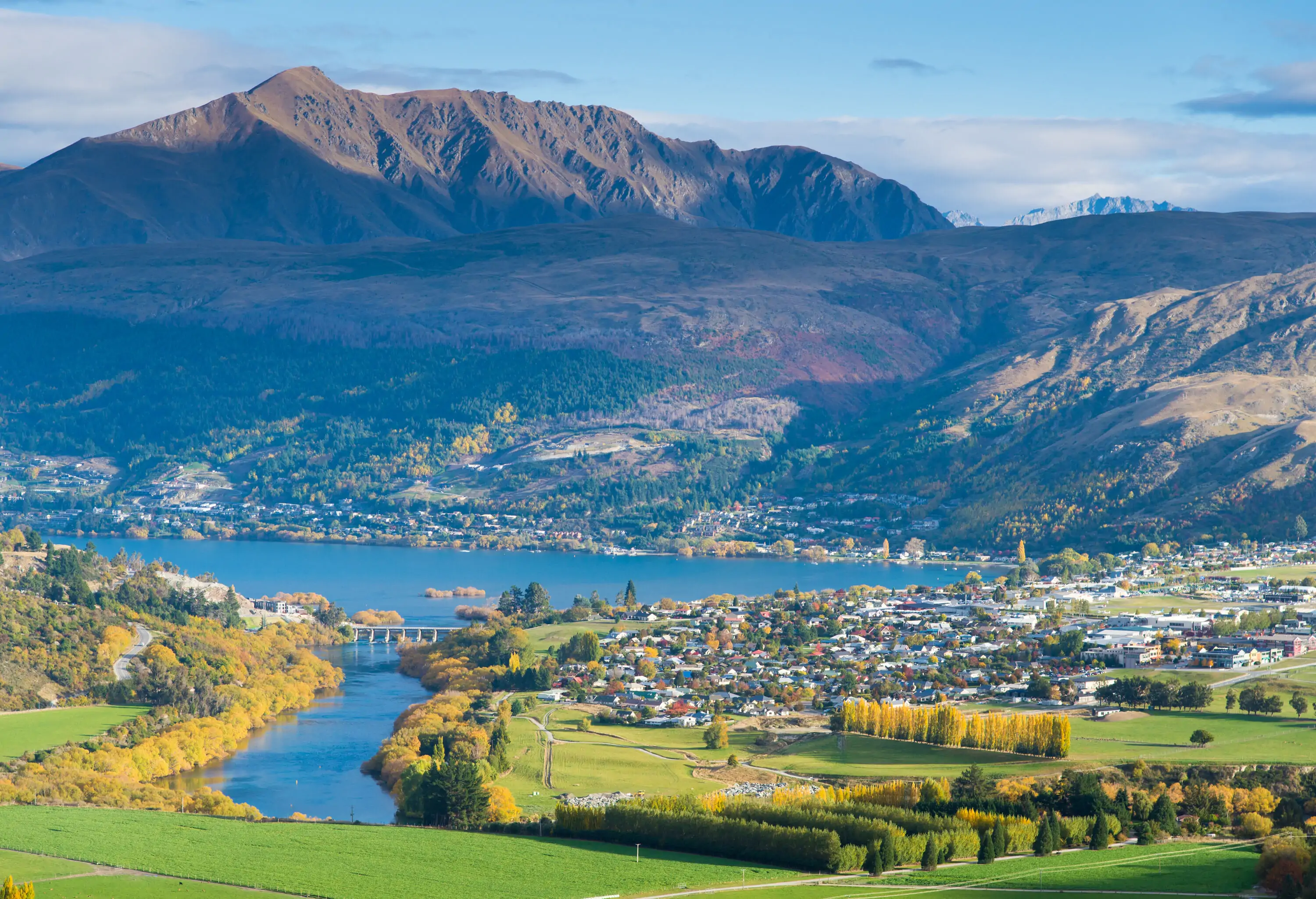 A lake, a nearby town, and the surrounding fall foliage against a forested mountain range.