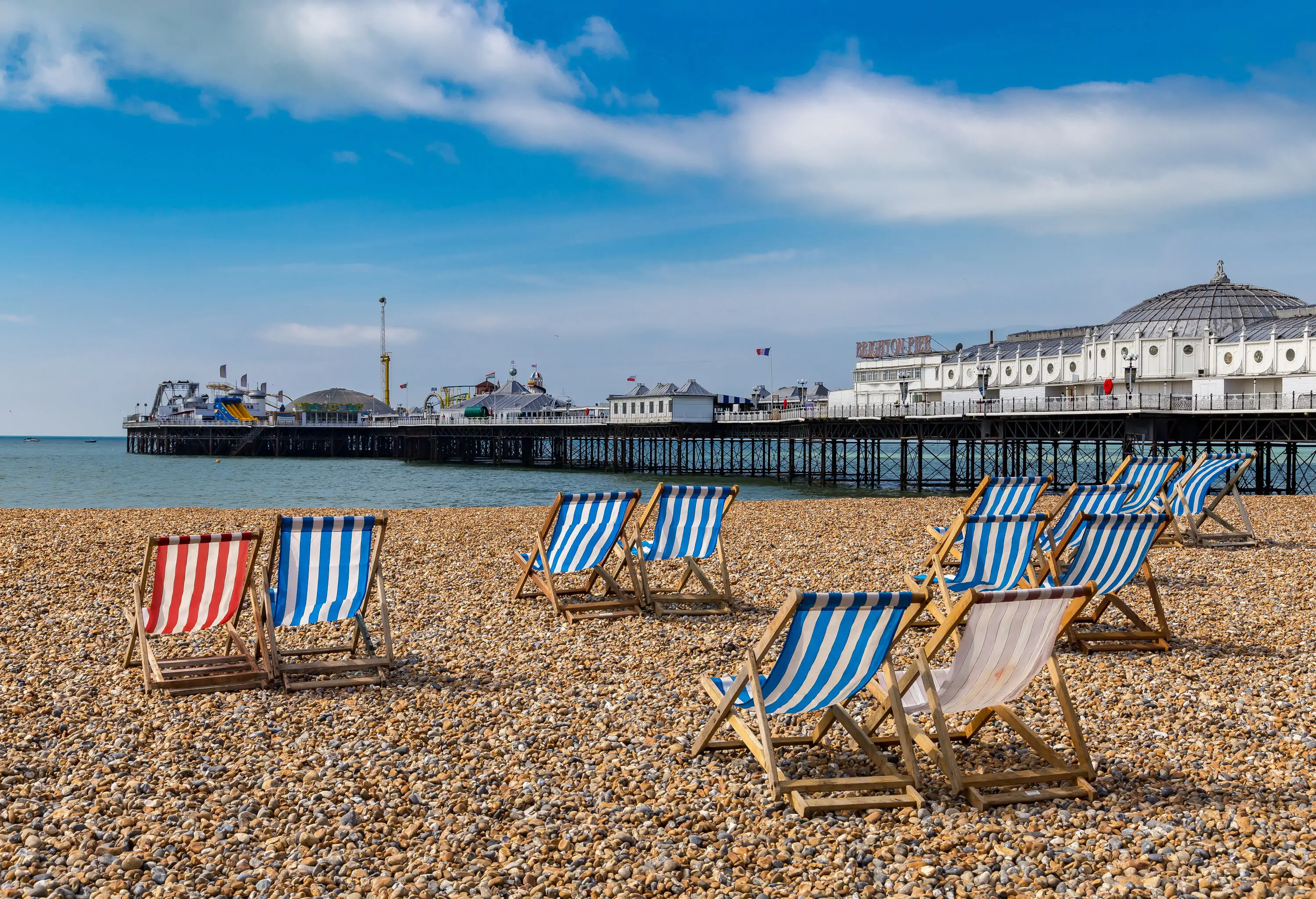 Colourful sunbeds with striped patterns set on a pebbled beach with views of an overwater pier.