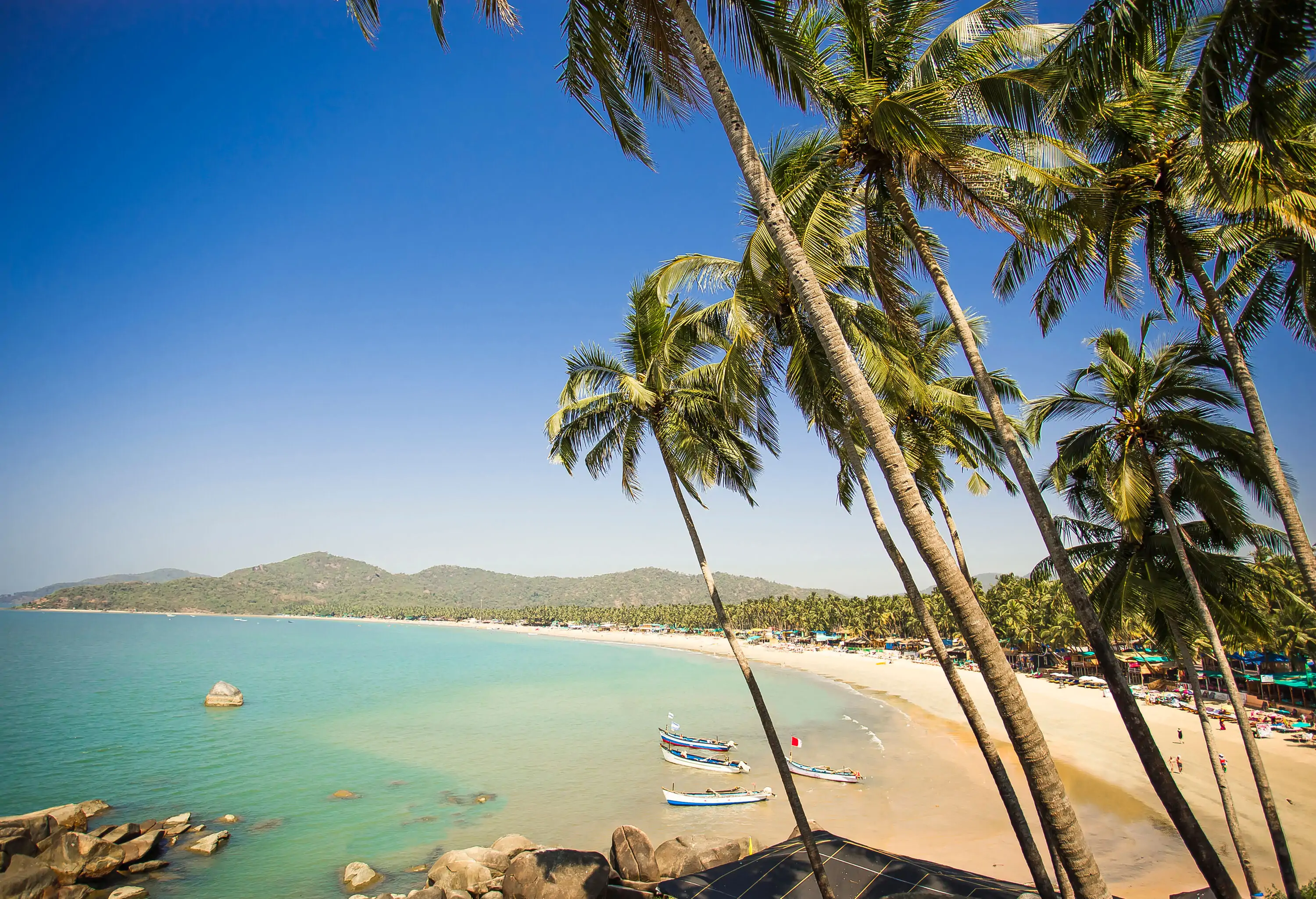 A long stretch of white sand beach surrounds the turquoise bay on a cloudless sky.