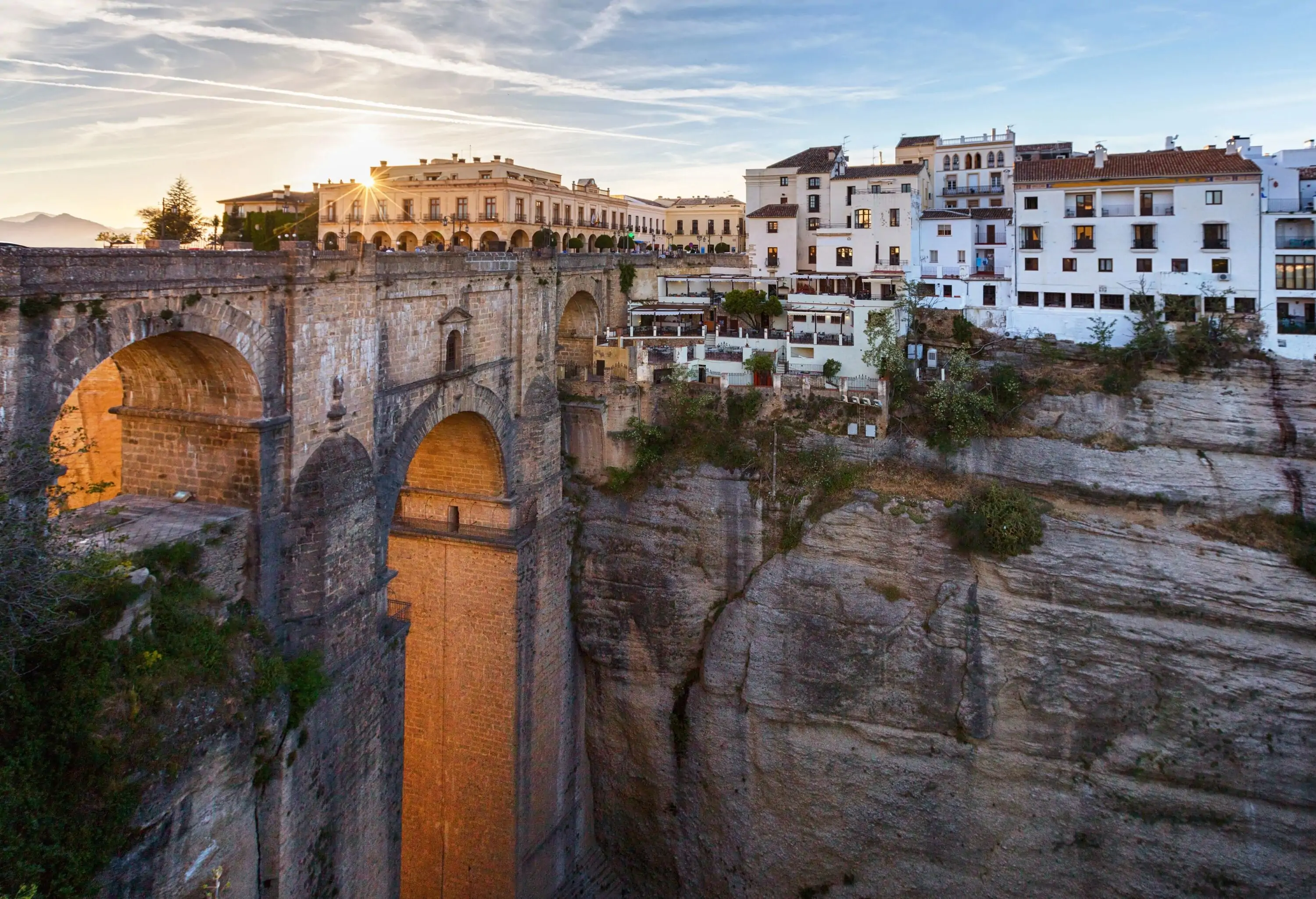 View of whitewashed andalusian village sitting atop a high drop mountain and high stone carved bridge