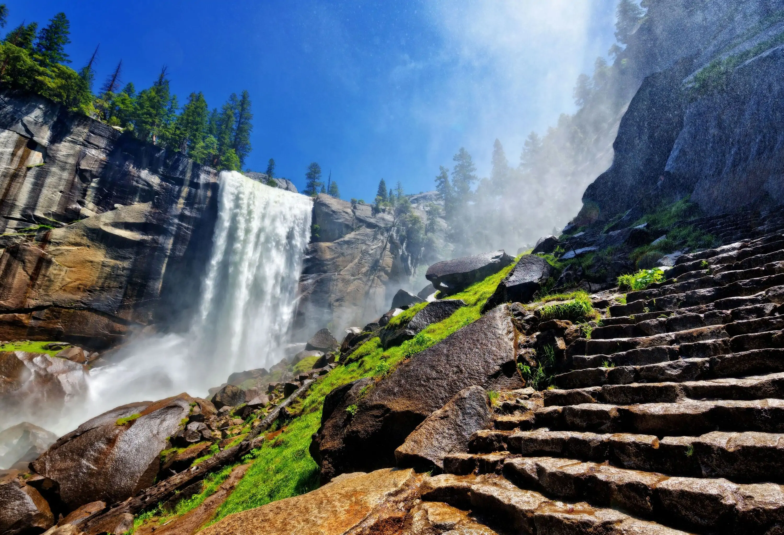 A staircase along the rocky slopes of a violent waterfall that pours from a steep cliff.