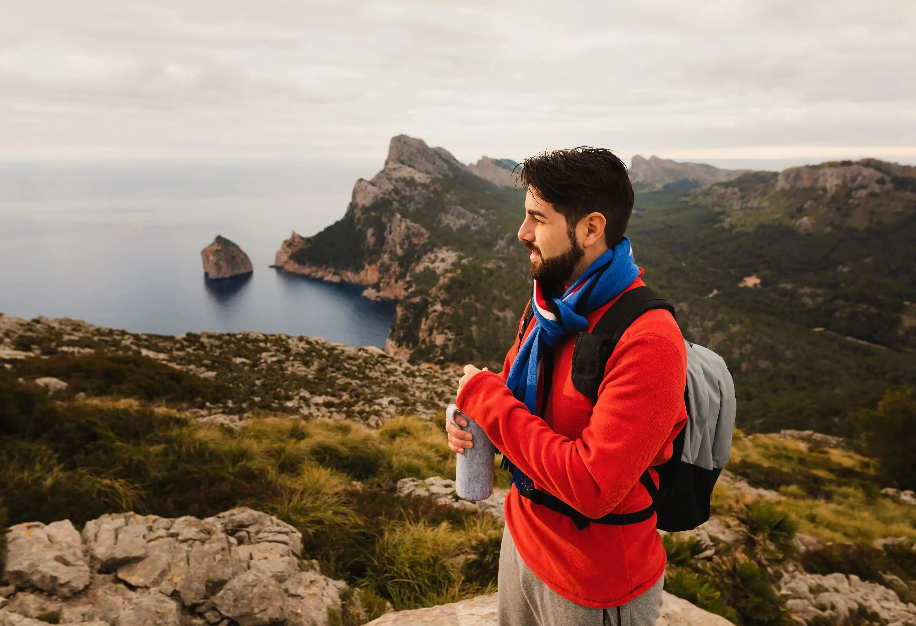 Young hiker standing on a high rock with his water bottle in the hands looking into the distance on the beautiful north coast of the island Majorca