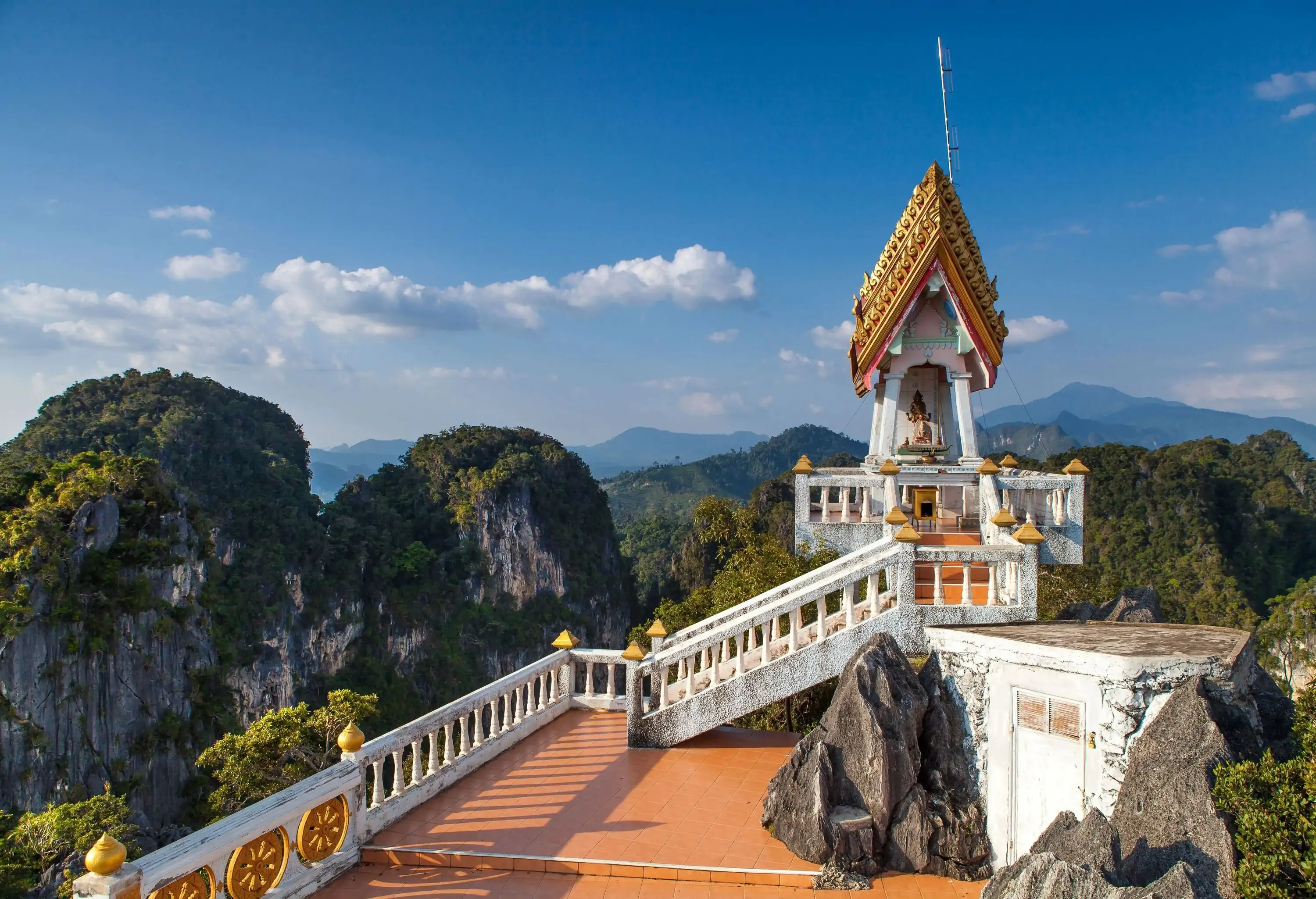 A view deck guarded by baluster with a statue on the pavilion overlooking lush mountains.