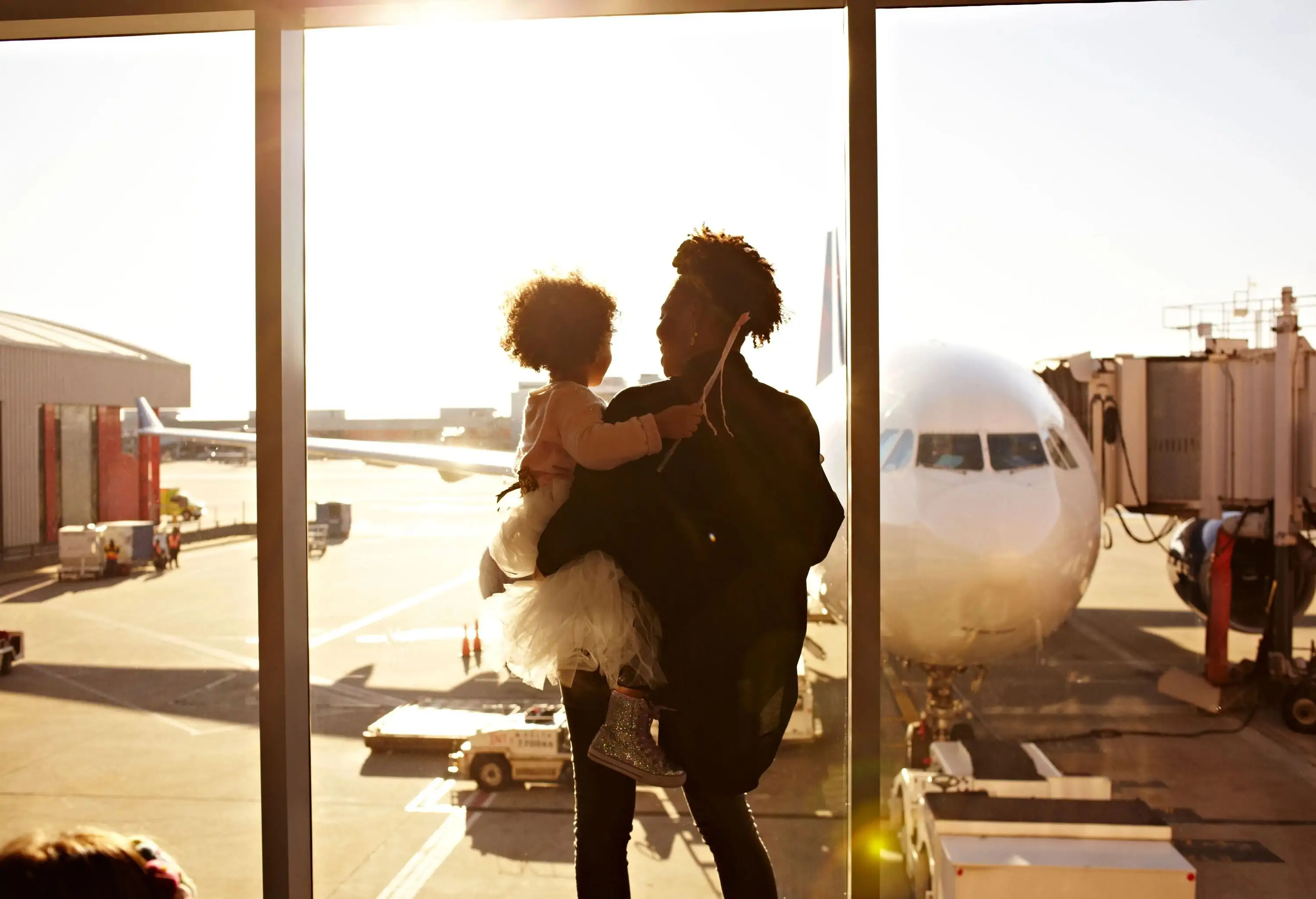 Mother holding daughter at airport looking at plane from a big window