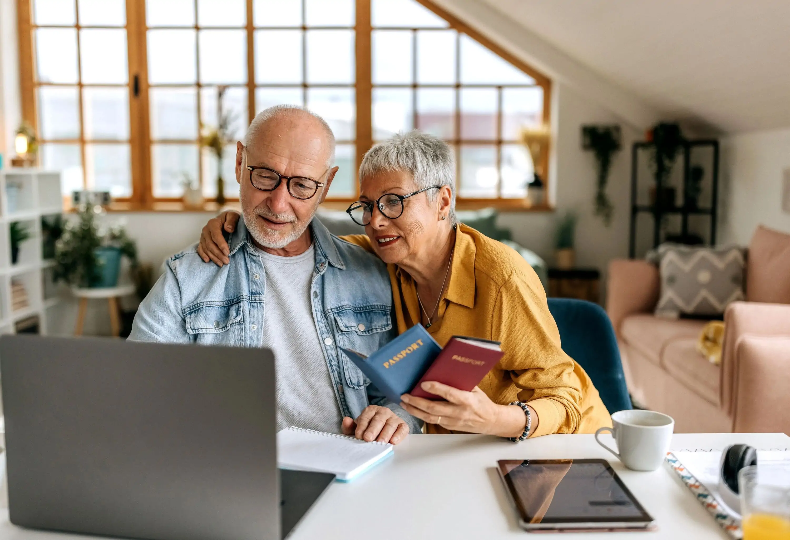 Senior couple booking their flight using laptop, holding passports in hand