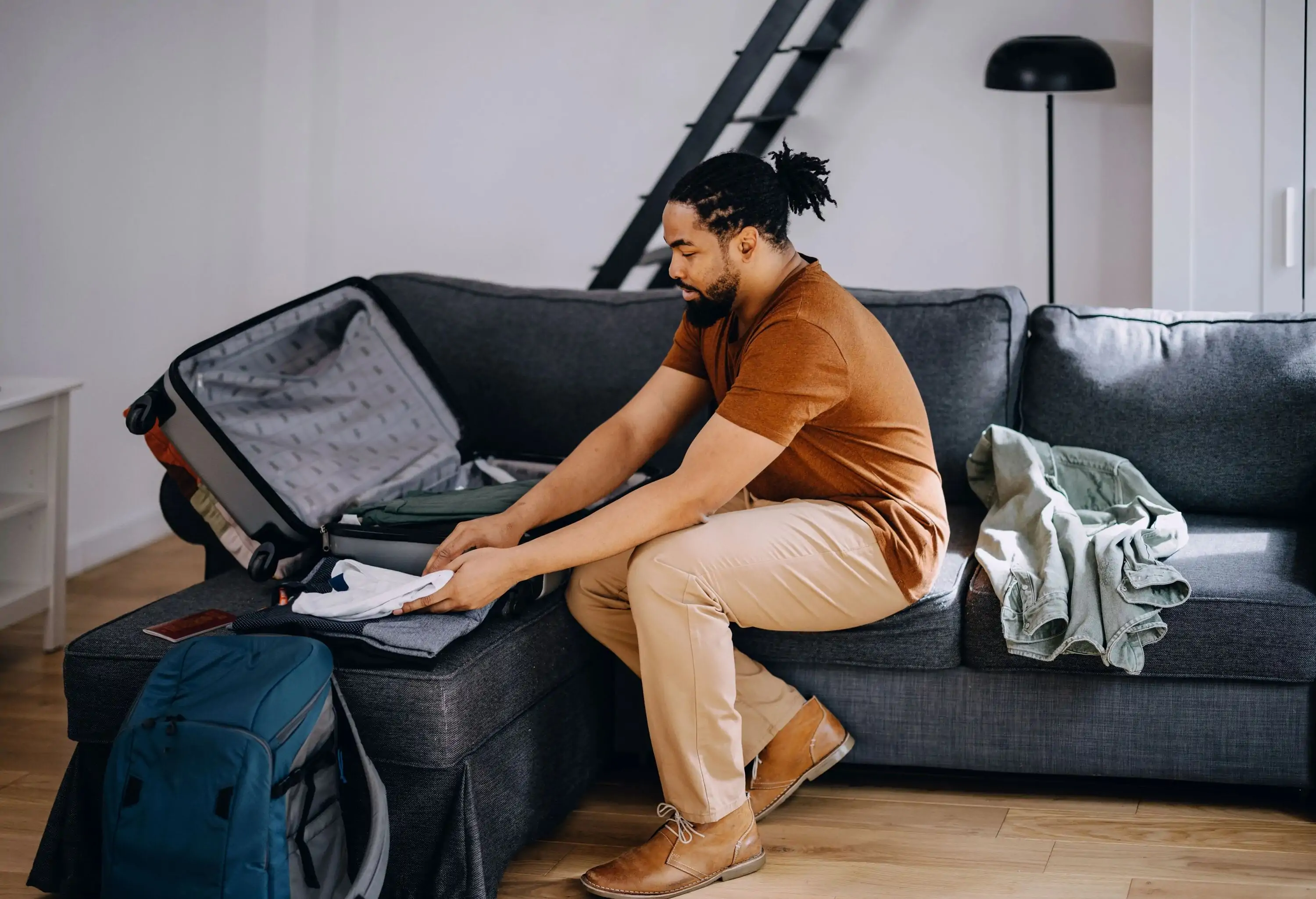 A smiling man packs clothes into luggage in his living area.
