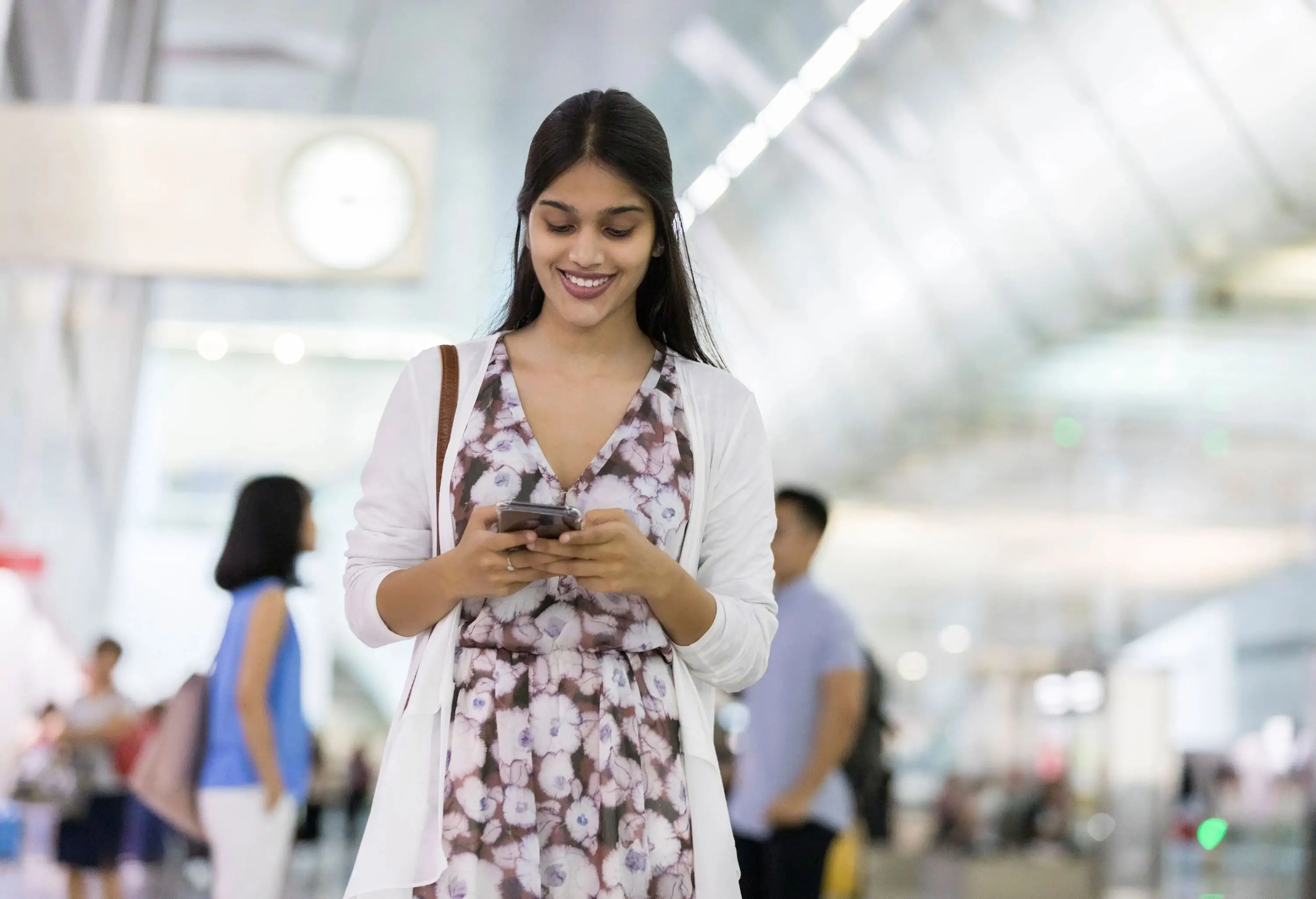 Young Indian woman uses smart phone while in airport. Travelers are in the background.