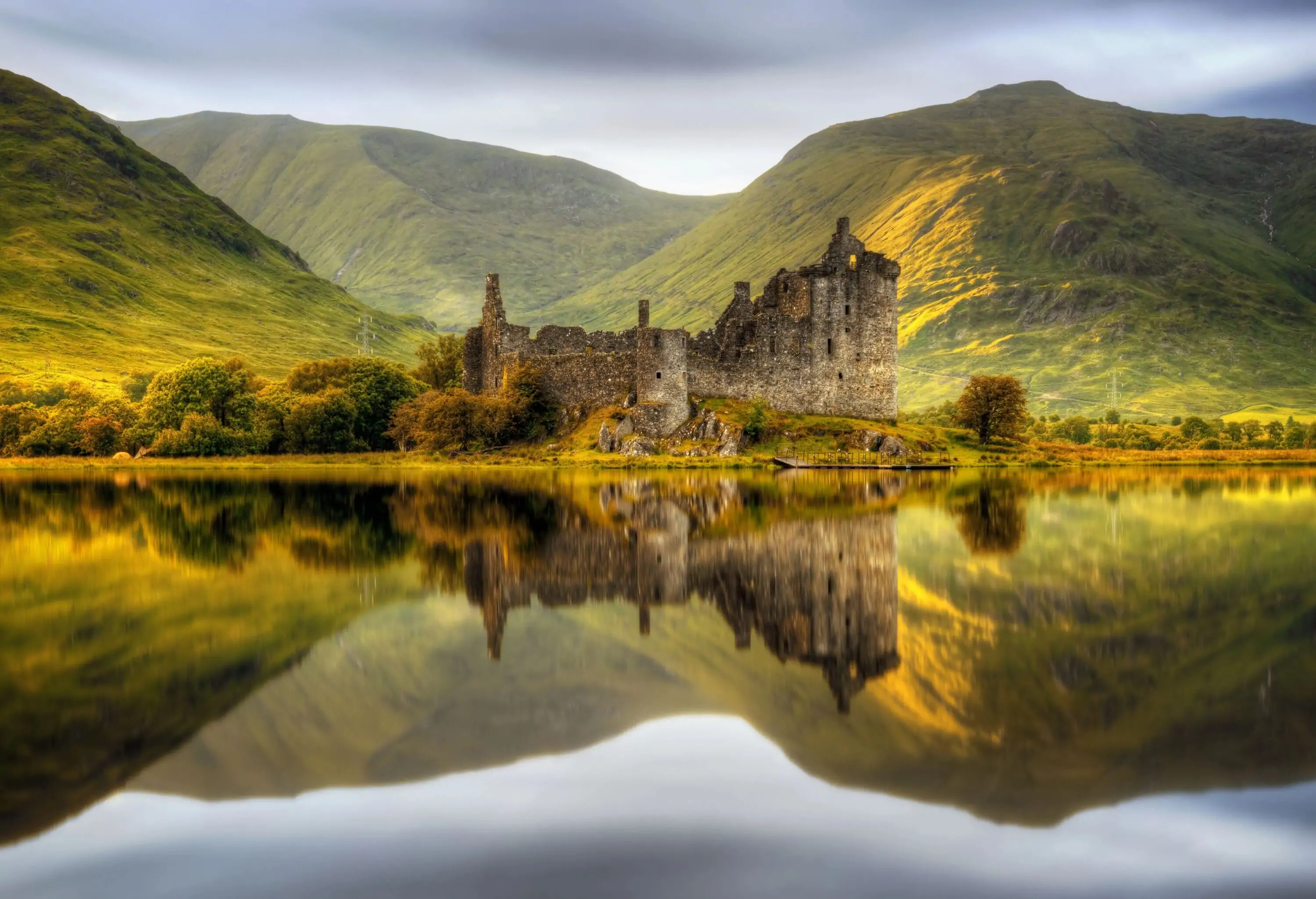 View of an ancient castle reflected in a lake with green hills in the background