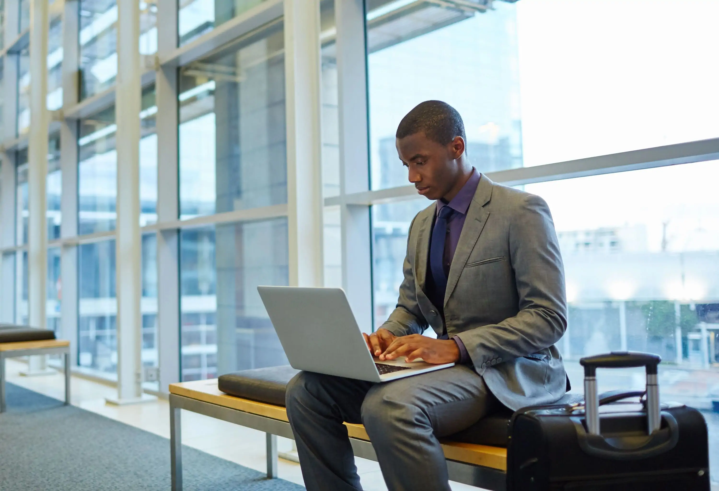 Shot of a young businessman sitting in an airport working on his laptop
