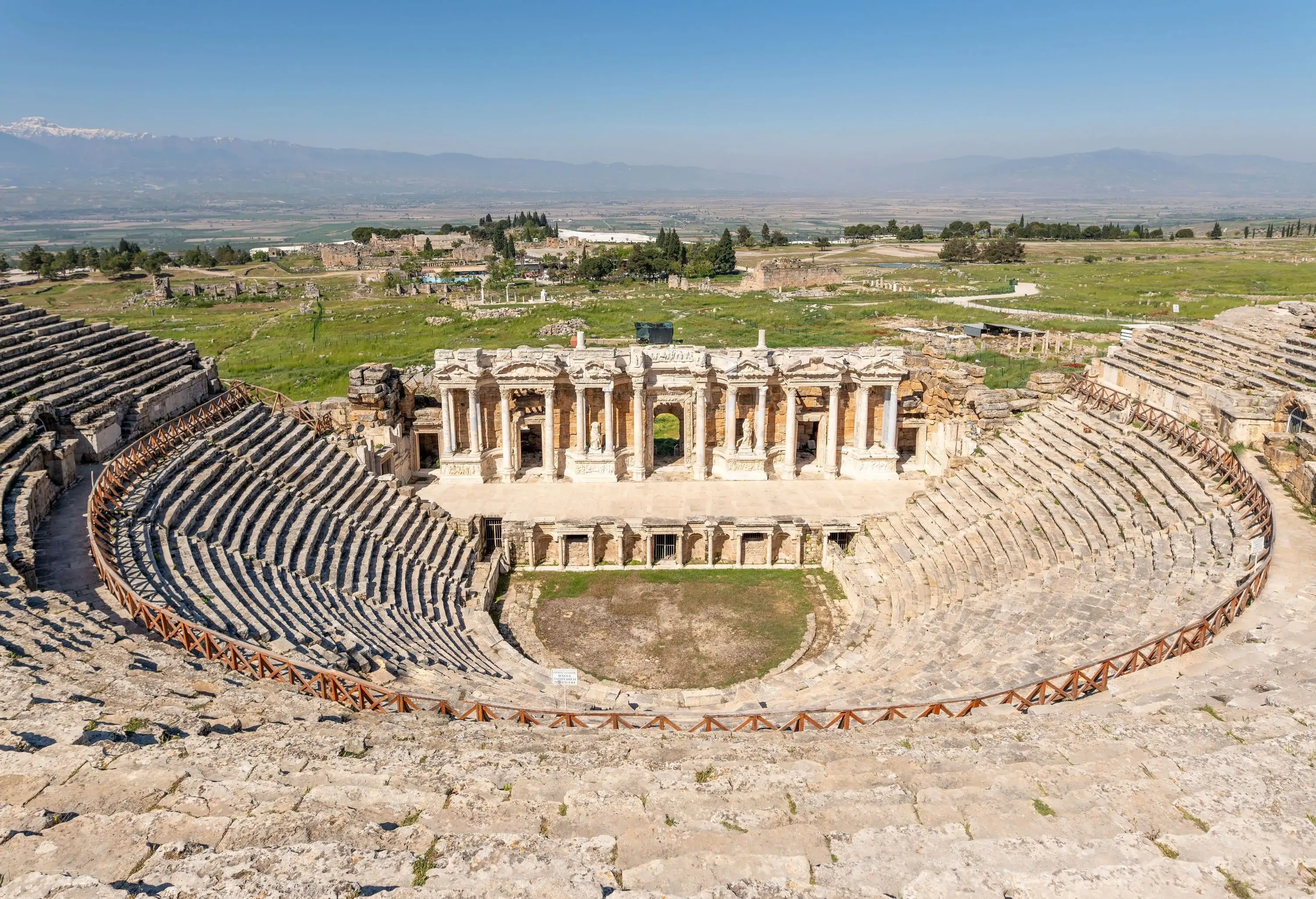 Ruins of an empty amphitheatre with tiered seating and a stage with pillared porticos.