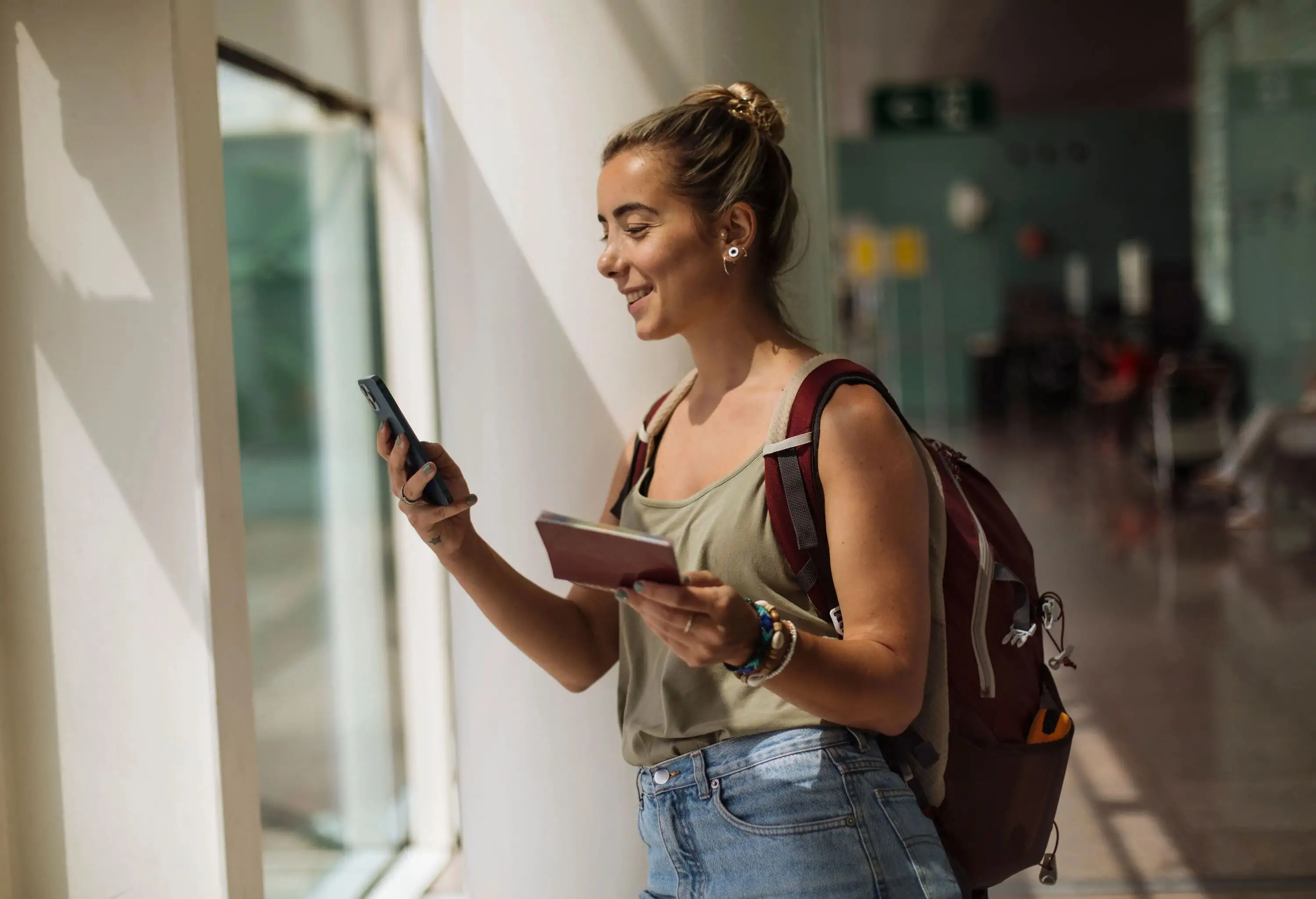 A young woman holding a phone and her passport is checking her flight reservation