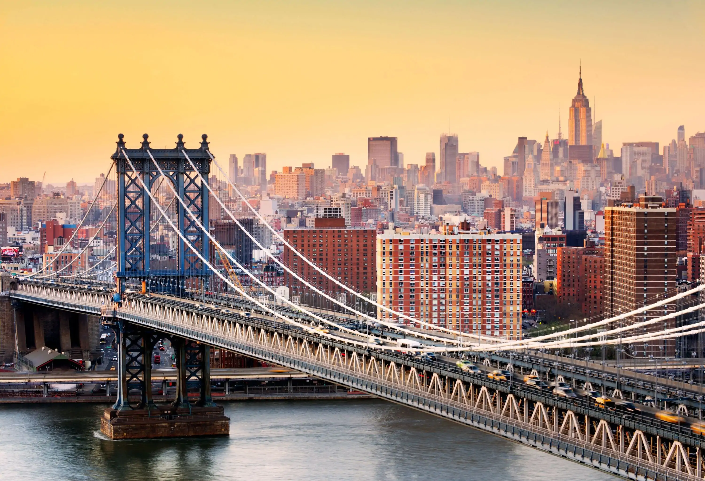 The beautiful Manhattan Bridge over the East River and New York landmarks accented with a soft yellow sky.