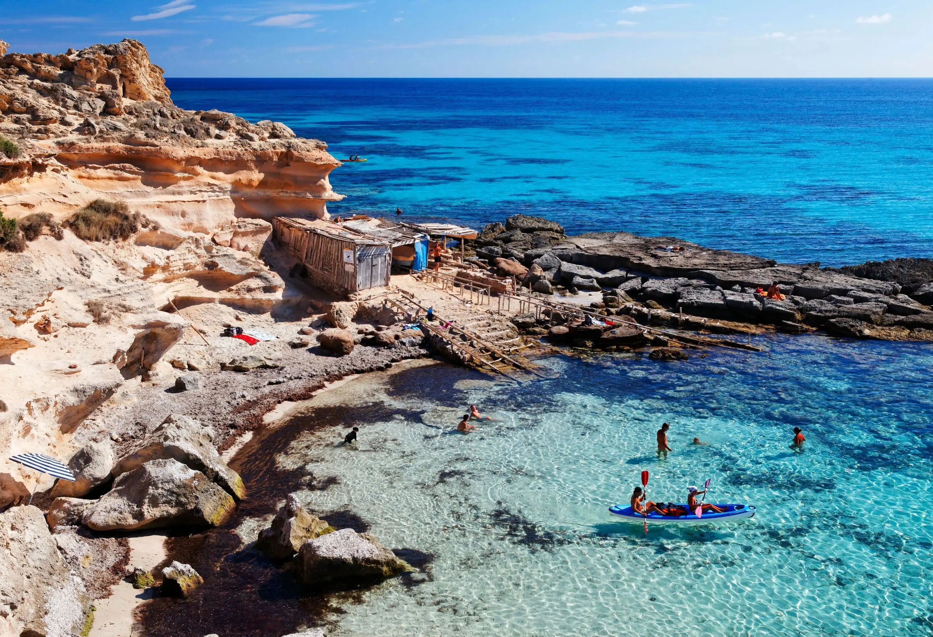 A rock cliff beside a natural pool with kayakers and people swimming.