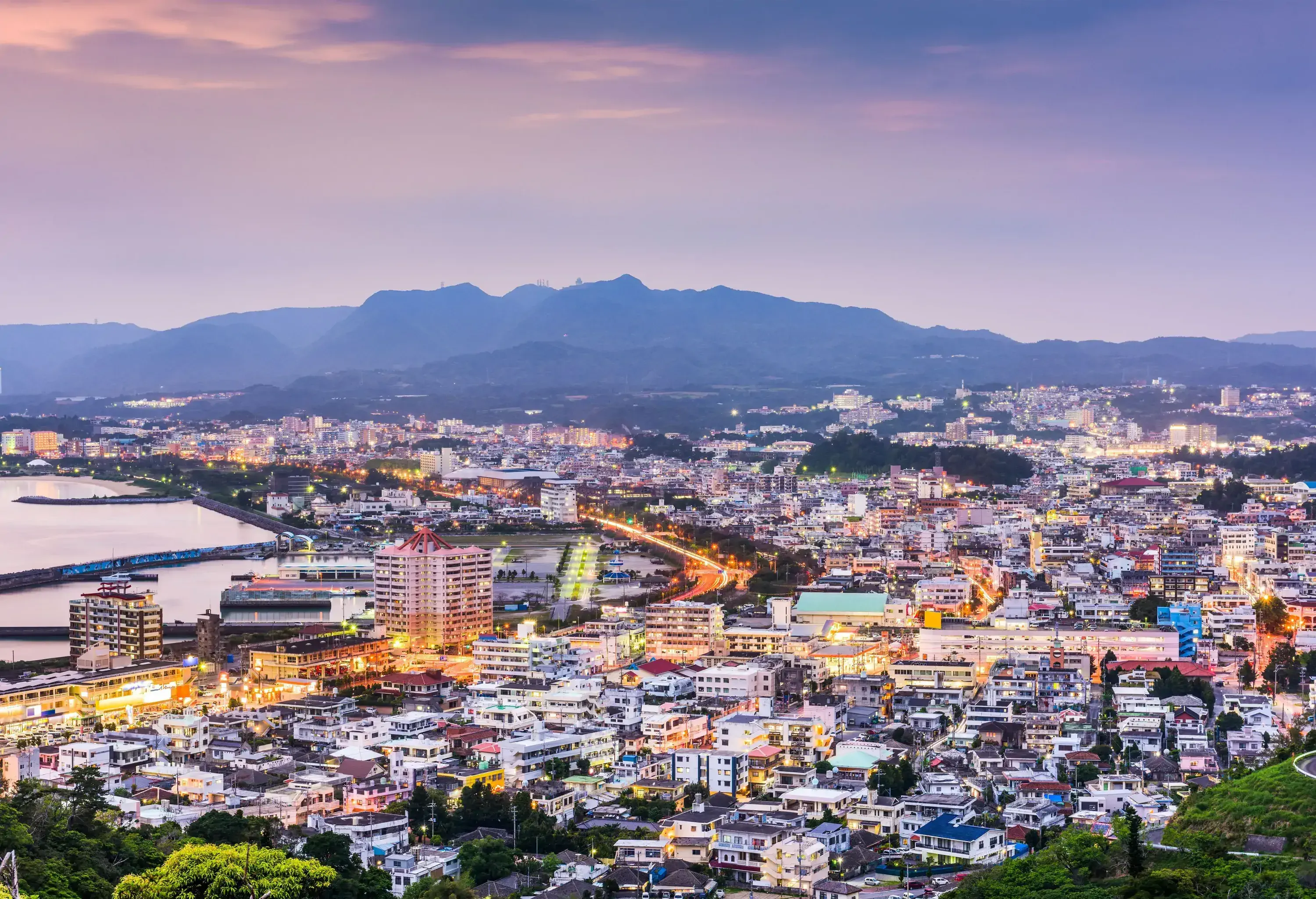 As dusk settles, a captivating cityscape comes alive with illuminated streets, while a majestic mountain range fades into the distance.