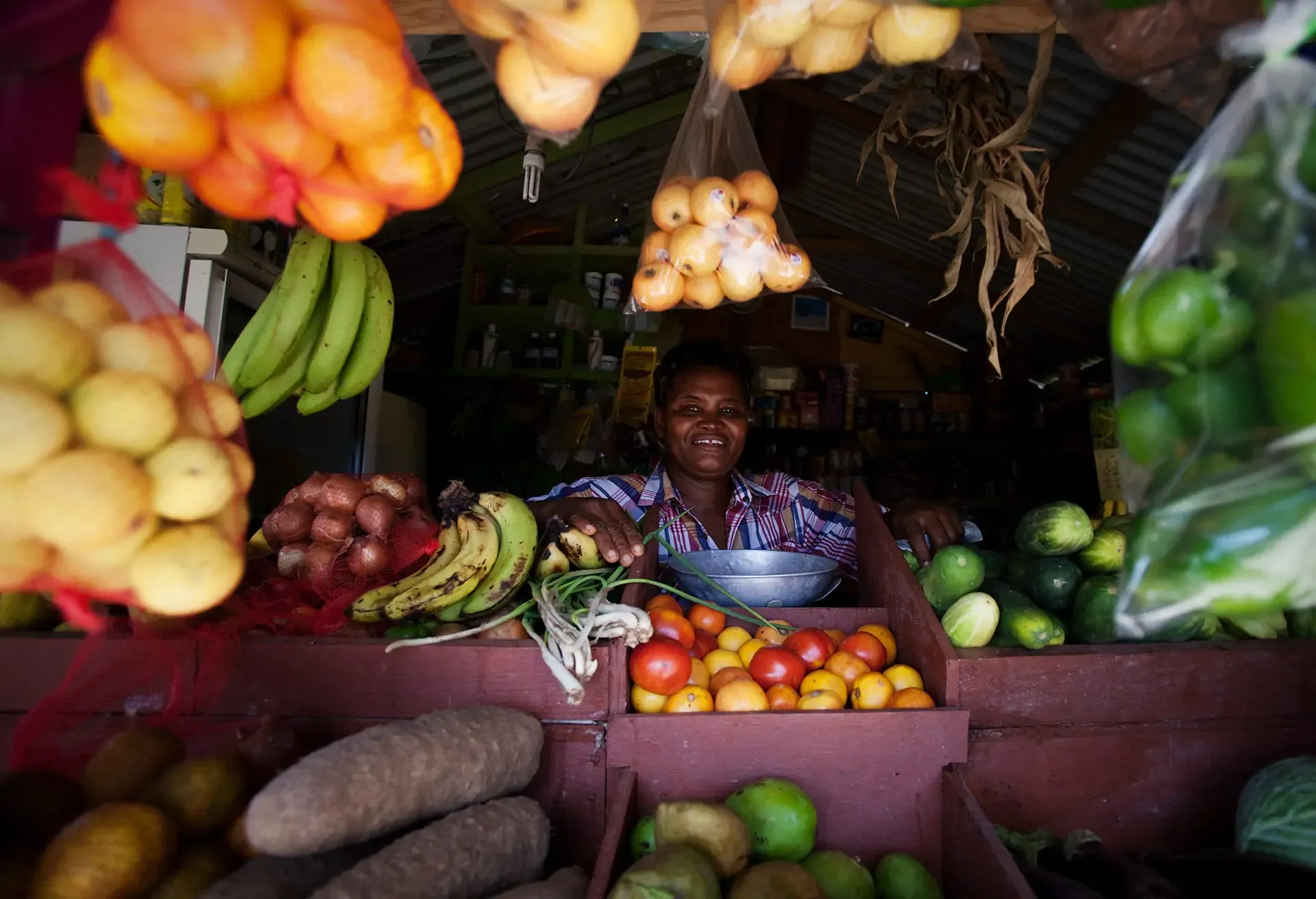 A smiling woman selling fresh fruits and vegetables at a vibrant local market stall.