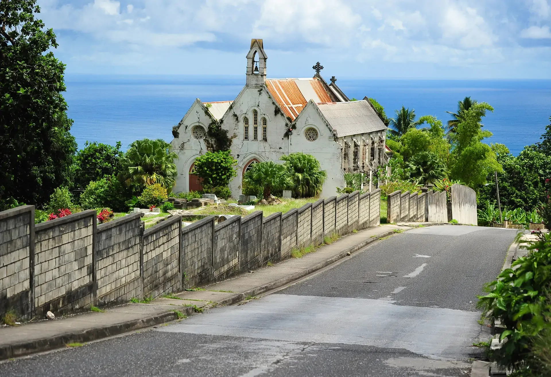 An old stone church on a hill overlooking the blue ocean under a cloudy sky.
