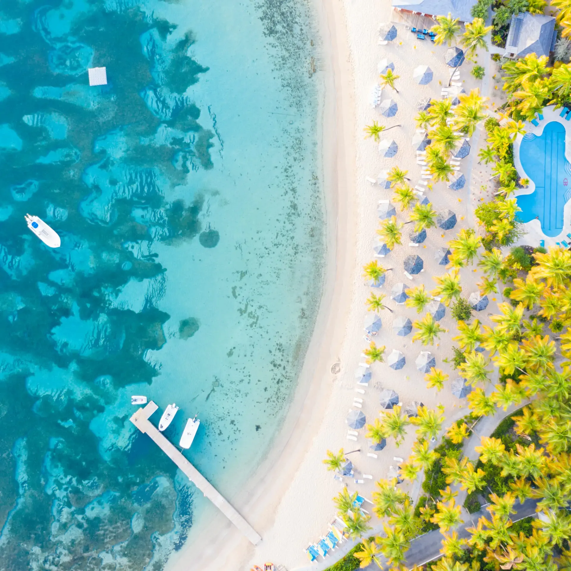 Aerial view of a tropical beach resort with turquoise water, white sand, and palm trees.