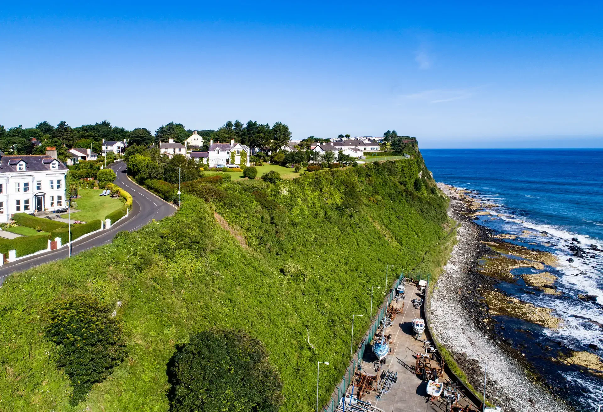 Atlantic coast with a steep cliff, marina and Causeway Coastal Road at Ballycastle, County Antrim, Northern Ireland, UK. Aerial view