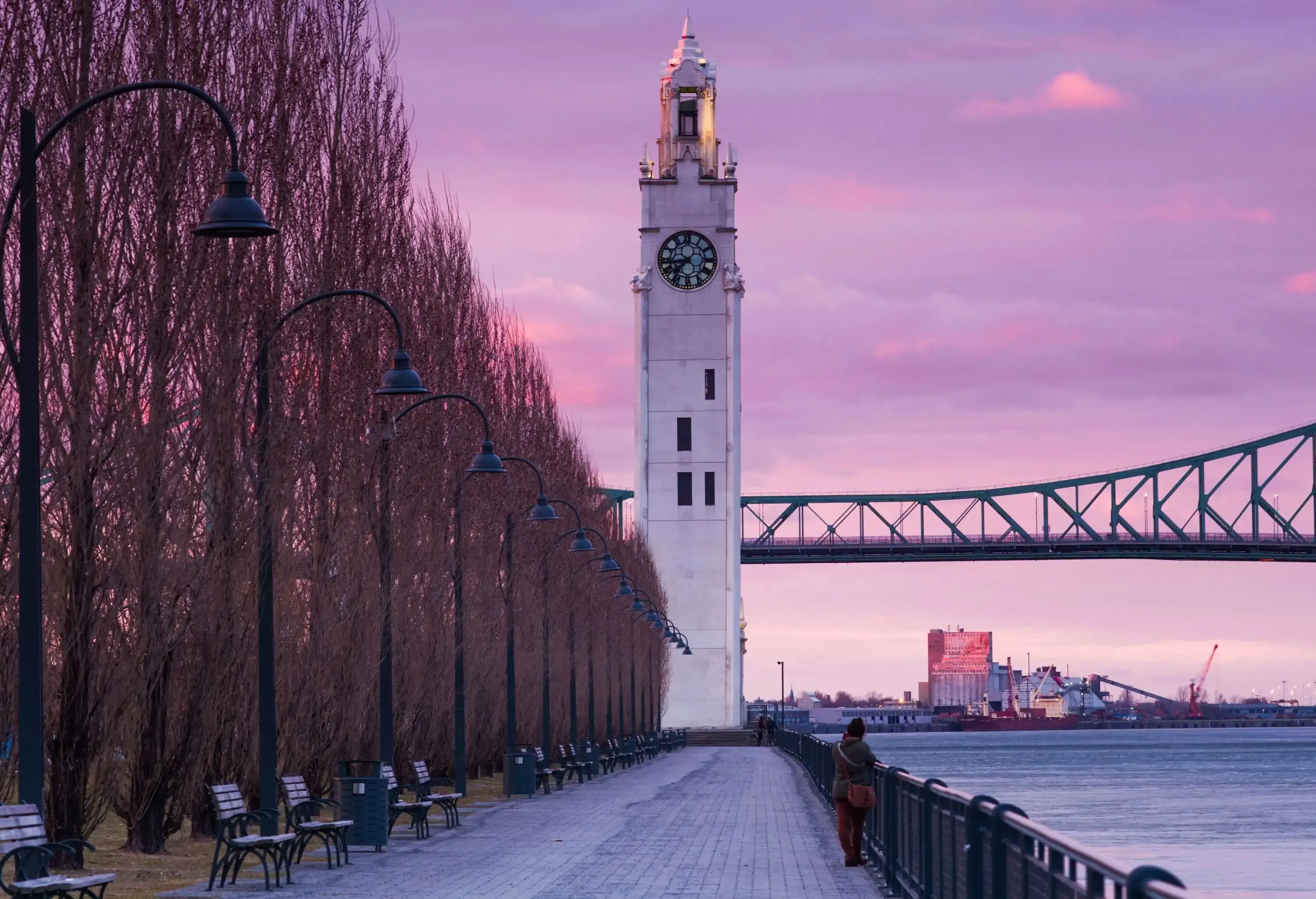 A woman standing on a promenade with the Old Port Clock Tower in the background. 