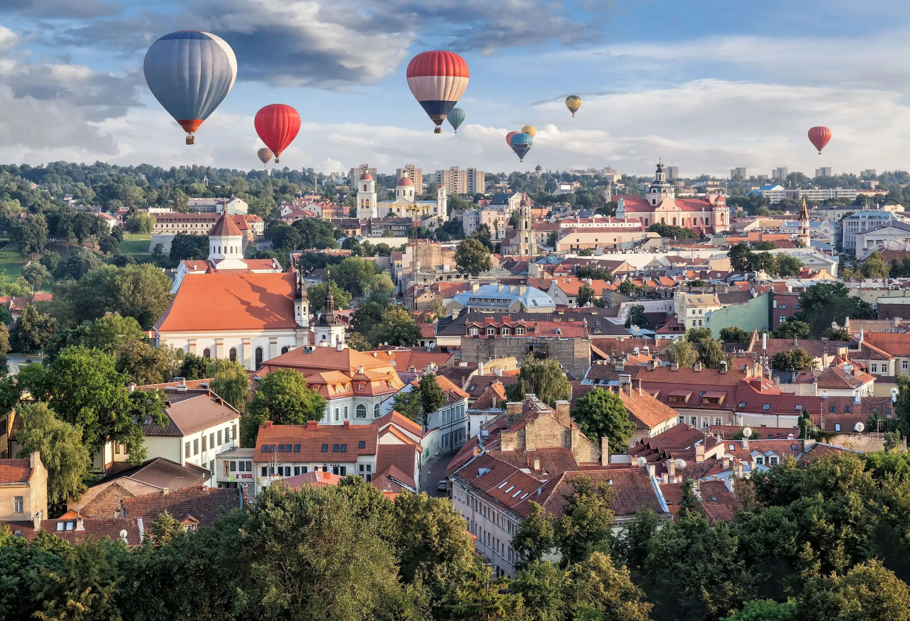 Urban landscape of a city with colourful hot air balloons floating above.