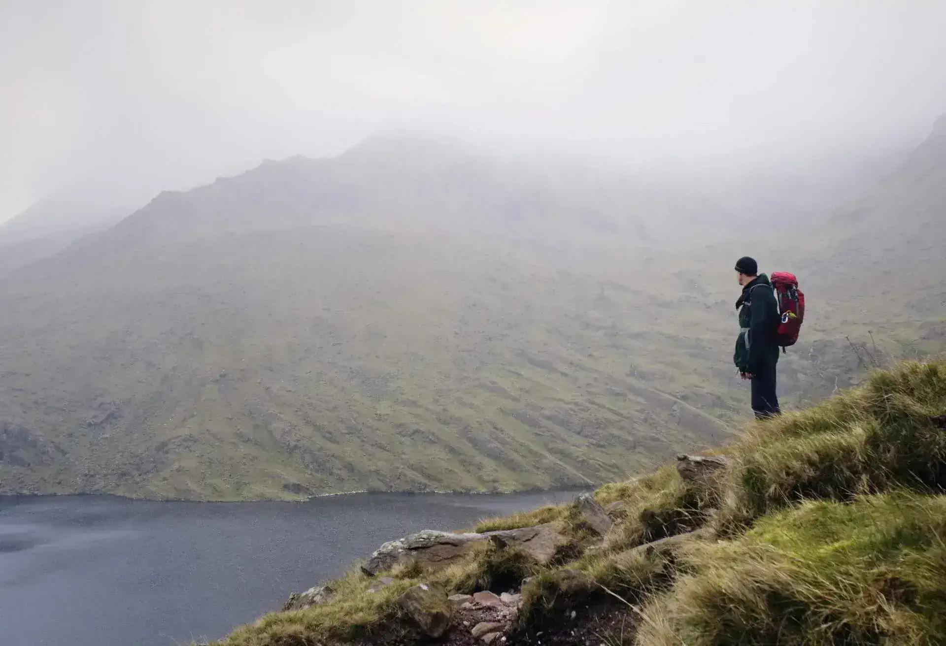 Hiker walking along a mountain trail in Ireland with sweeping views of valleys and peaks.