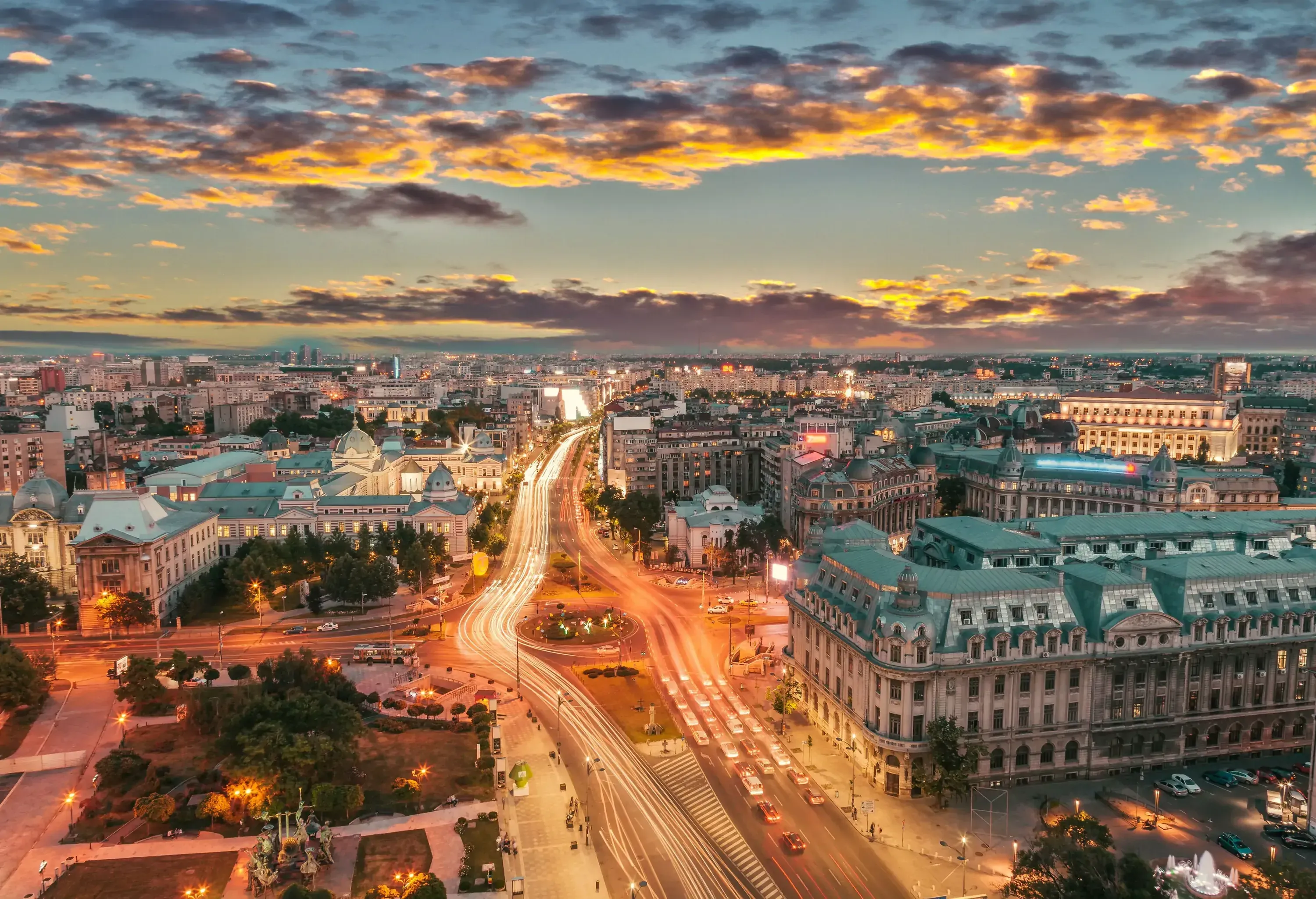 Vehicle light trails making the roadways glow as they wind among the city buildings beneath a dreary sky.