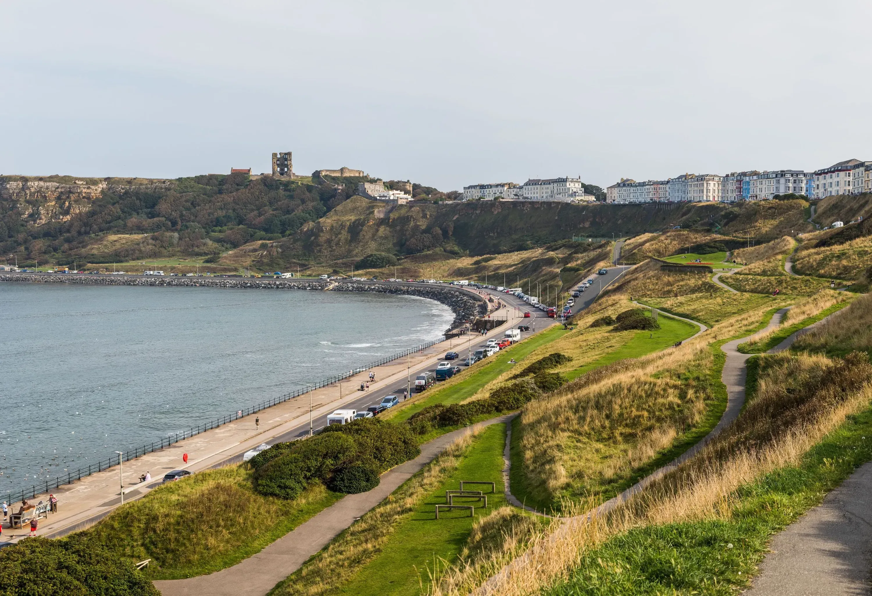 Pathways on the hillside gracefully lead down to the bay, with a charming promenade below and waterfront buildings standing proudly along the stretch of the cliff.