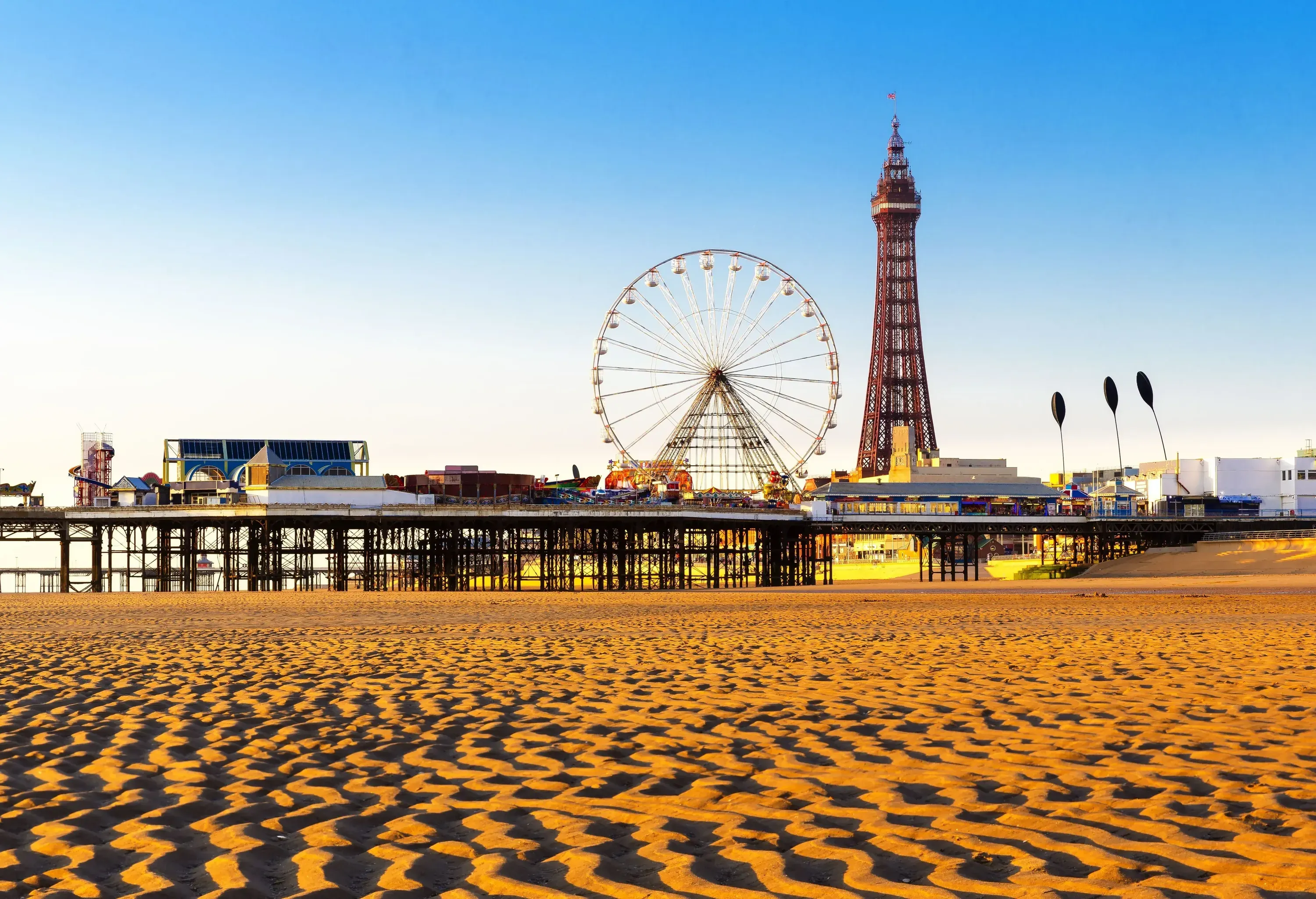 A beach with pronounced seabed grooves and a pleasure pier in the distance.