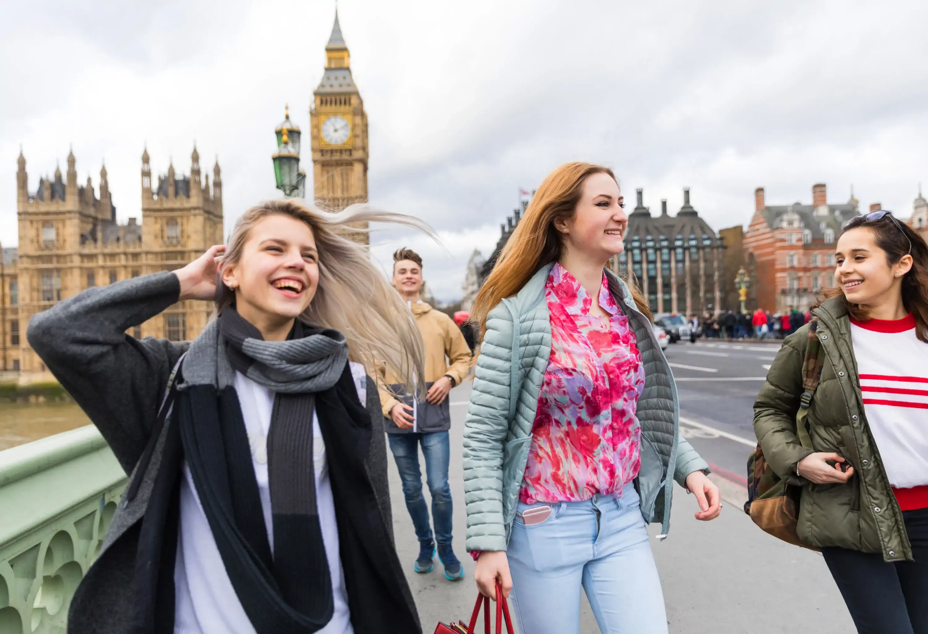 Four happy young individuals are on a bridge against the iconic Big Ben, a historic clock tower in London.
